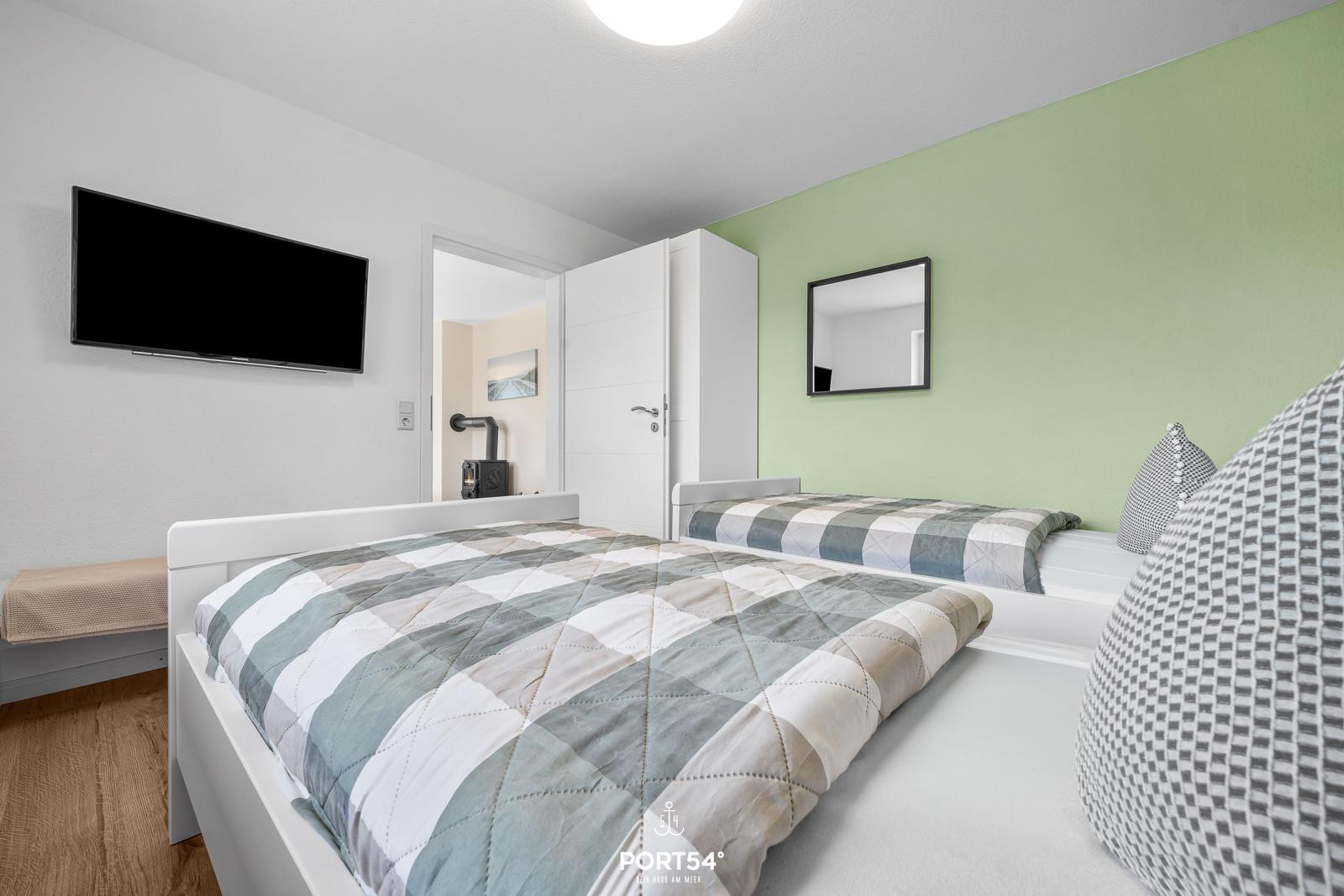 Zwei Betten mit gemusterten Bettwäsche, Wandspiegel und Fernseher an der Wand.