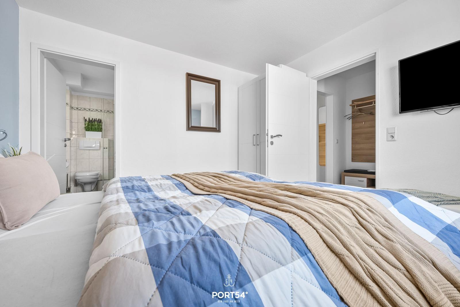 Schlafzimmer mit Bett, Fernseher und Blick in Bad und Kleiderschrank.
