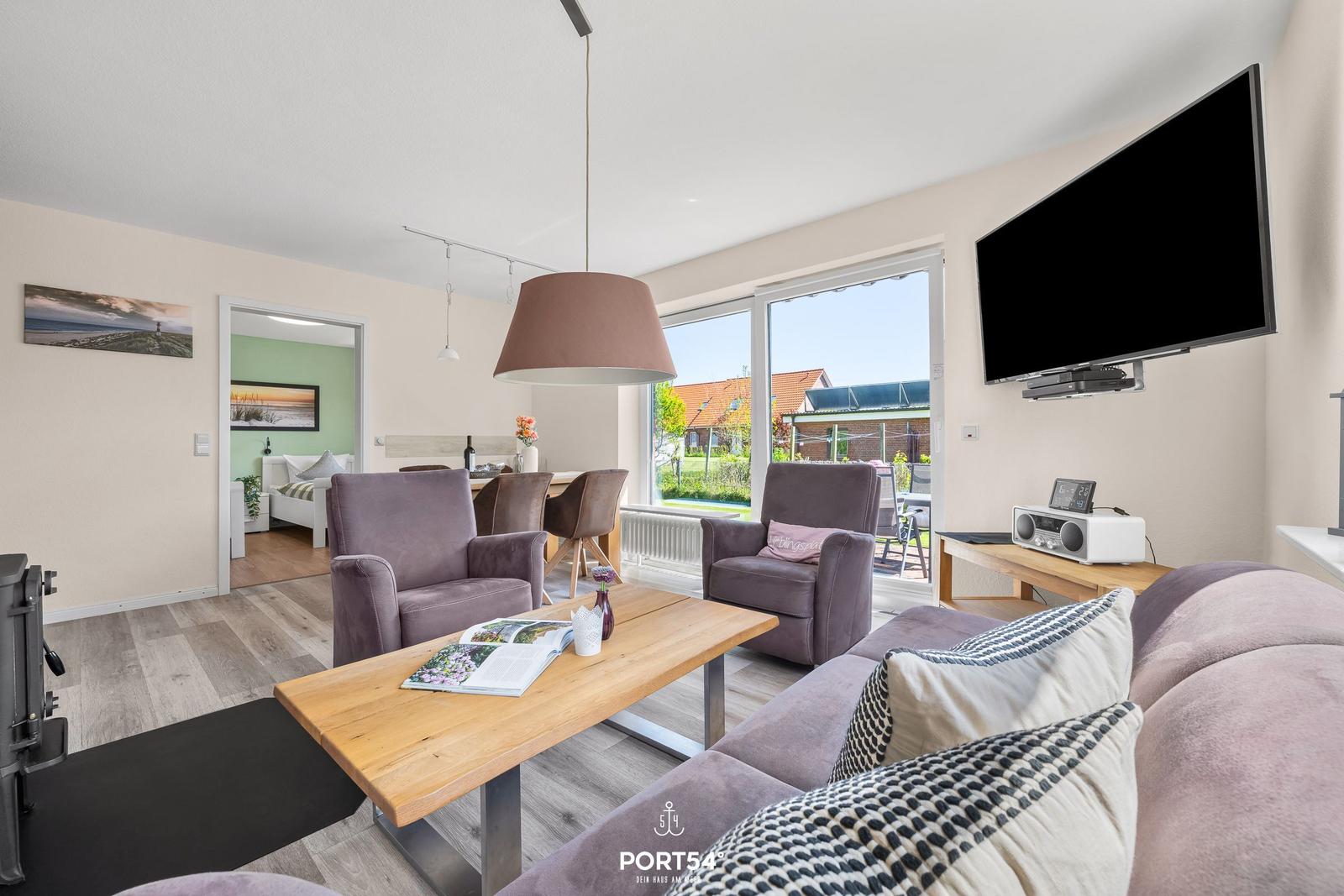 Wohnzimmer mit Sofa, Sesseln und TV. Durchgang in Schlafzimmer. Blick auf Garten.