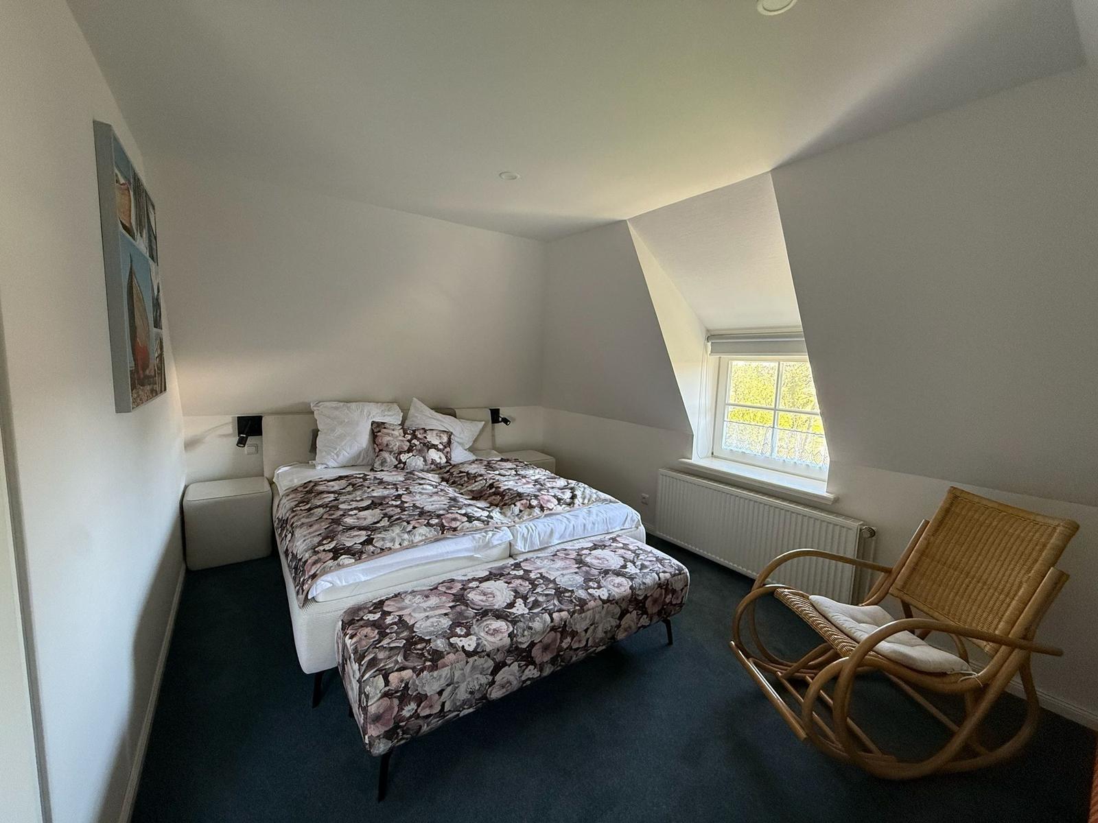 Schlafzimmer mit Doppelbett, Schaukelstuhl und Dachfenster.
