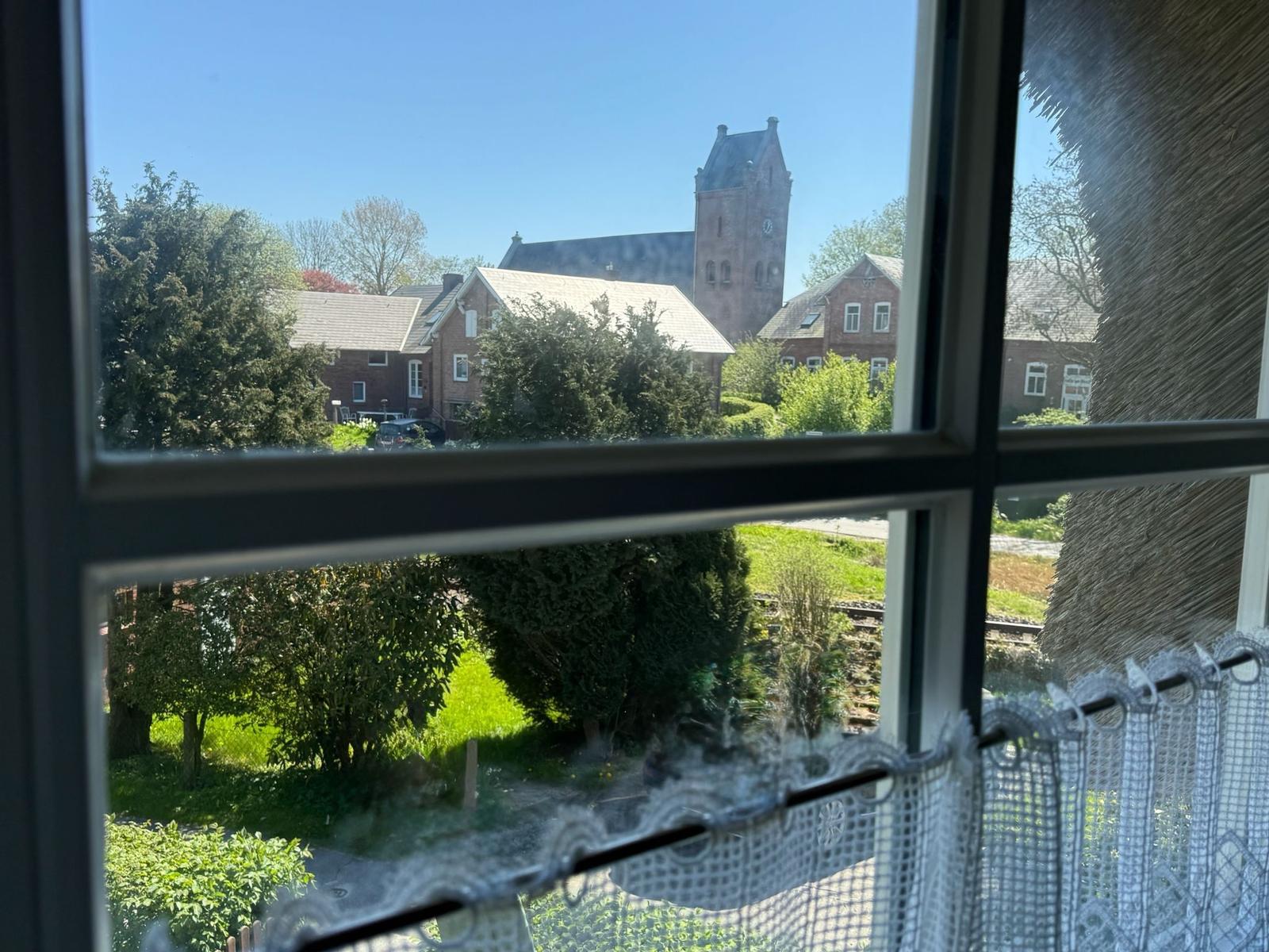 Durch das Fenster ist eine Straße mit Bäumen und einem Kirchturm zu sehen.