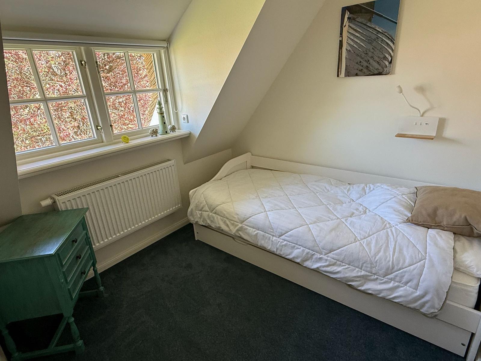 Ein Schlafzimmer mit Dachschrägen, einem Bett, einem grünen Nachttisch und einem Fenster.
