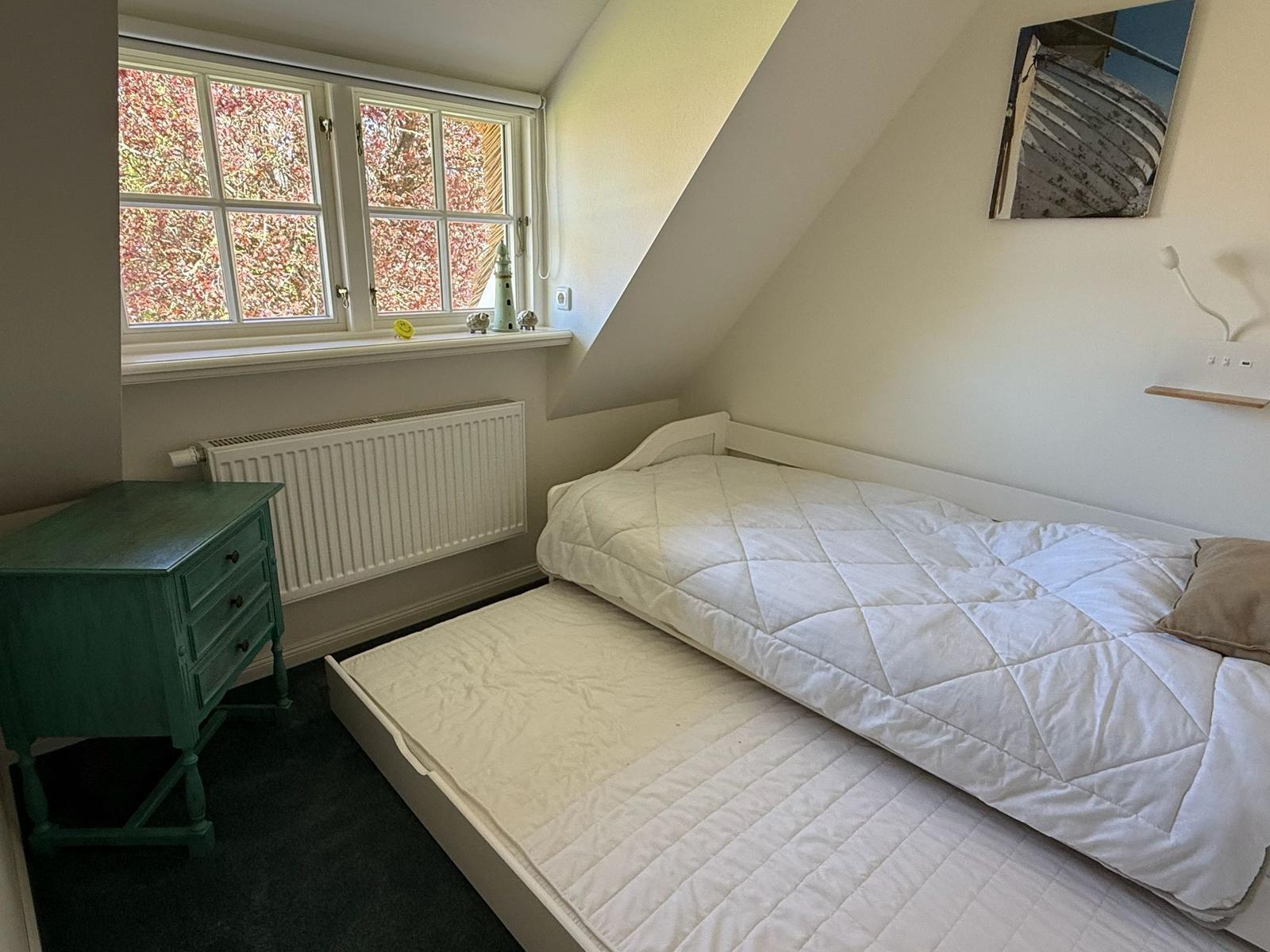 Schlafzimmer mit Doppelbett, grünem Nachttisch und Fenster mit Blick auf Bäume.