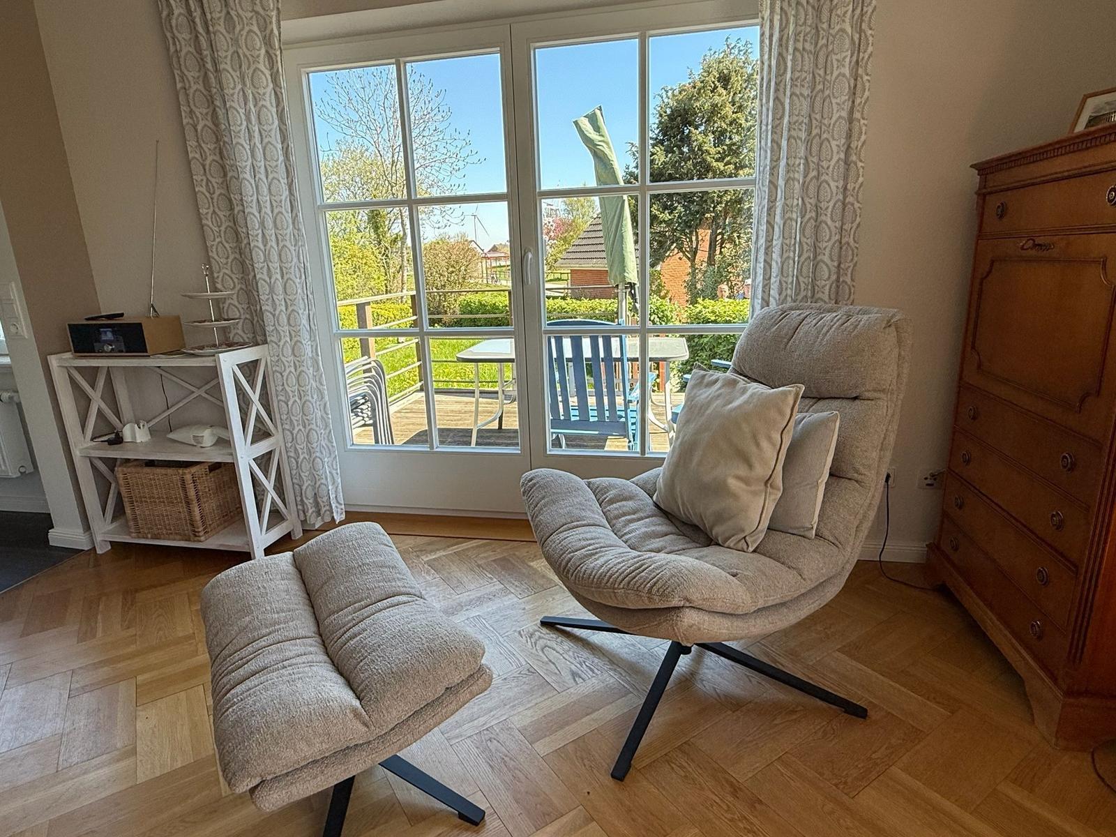 Ein Raum mit Sessel, Fußstütze und Schrank. Durch das Fenster ist eine Terrasse zu sehen.