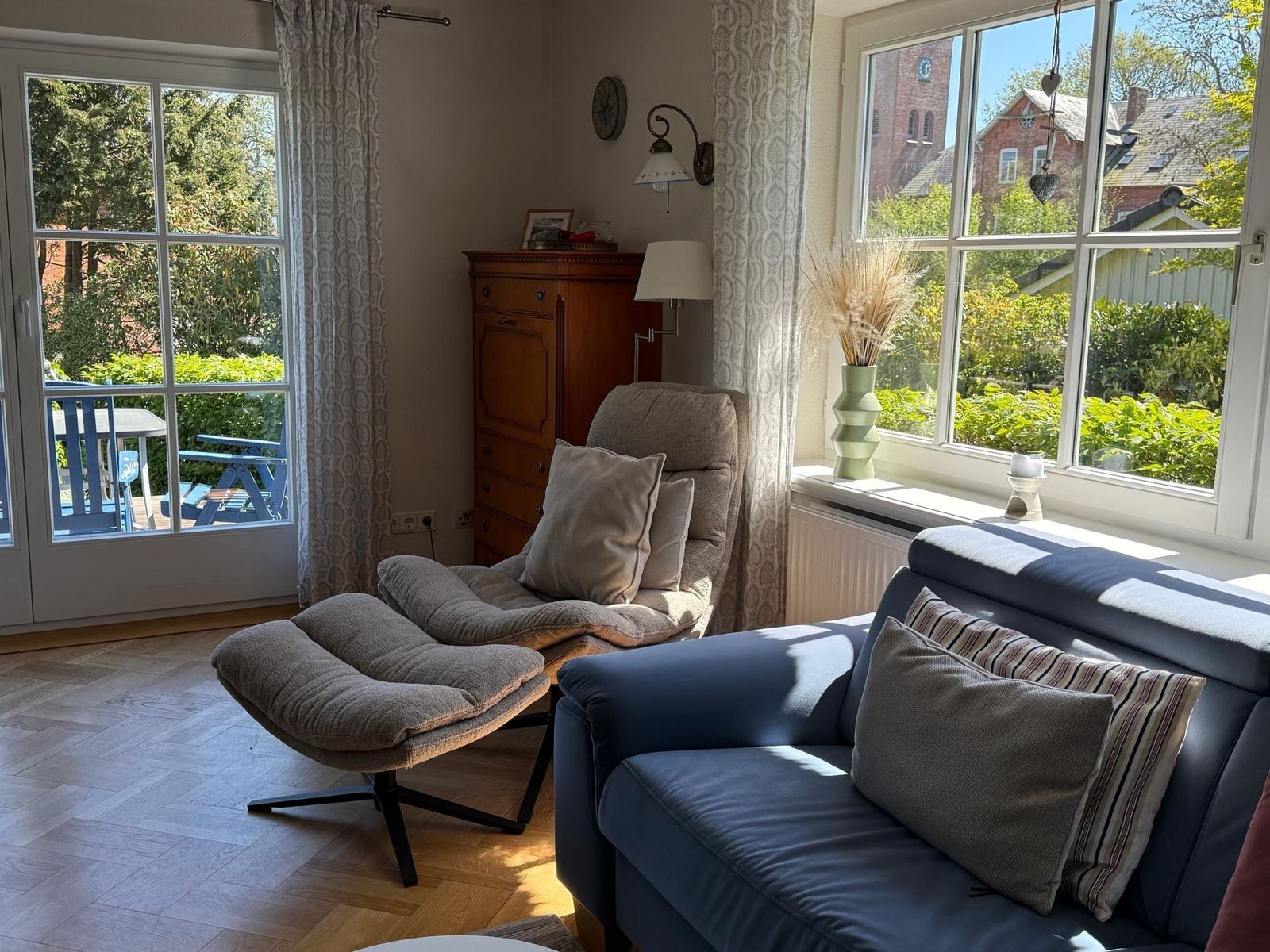 Ein Wohnzimmer mit Sofa, Sessel und Fenstern zum Garten.