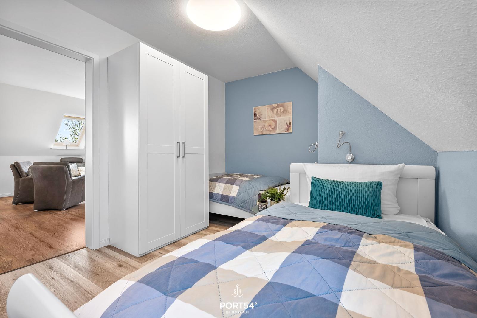 Schlafzimmer mit Dachschrägen, weißer Kommode und Bett mit blau-beigem Quilt.