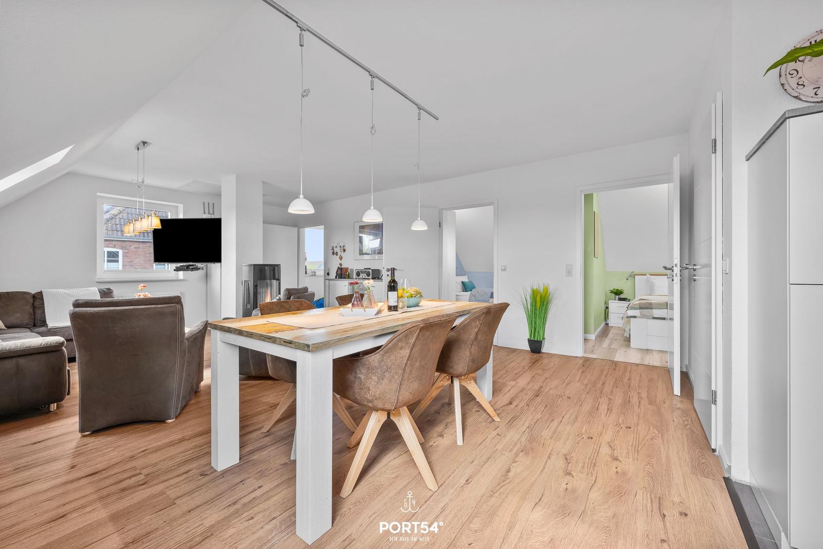 Wohn- und Essbereich mit Holzboden, Esstisch und Sofa. Im Hintergrund ist ein Schlafzimmer sichtbar.