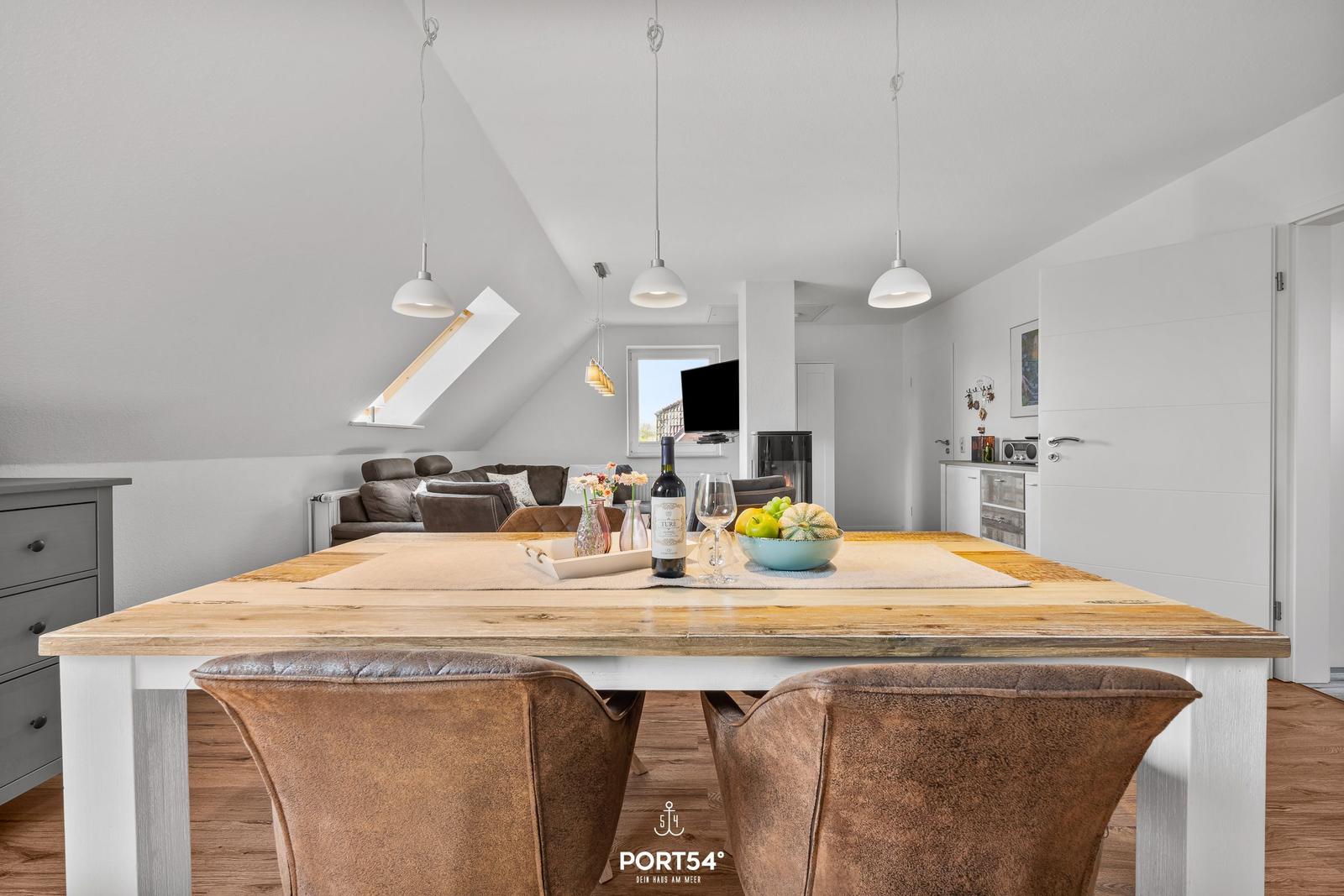 Essbereich mit Holztisch und Ledersitzen. Im Hintergrund Wohnbereich mit Sofa und Fernseher.