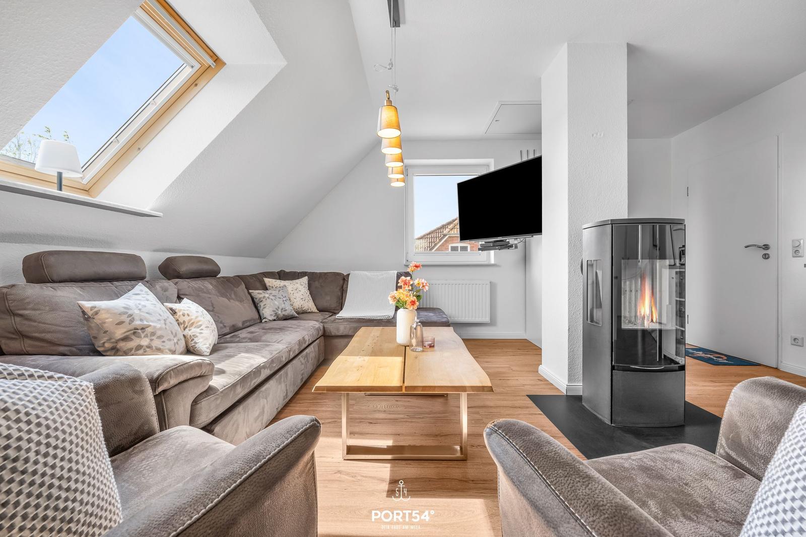 Wohnzimmer mit Sofa, Couchtisch und Kaminofen unter Dachschrägen.