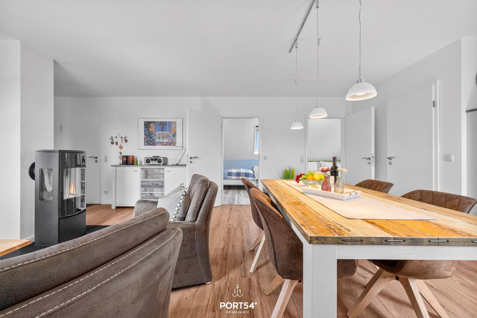 Essbereich mit Holztisch und Stühlen. Im Hintergrund Wohnbereich mit Kamin und Schlafzimmer.