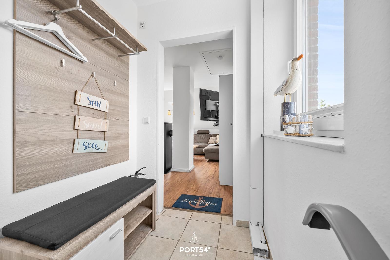 Eingangsbereich mit Kleiderhaken, Sitzbank und Blick in Wohnzimmer mit Sofa und Fernseher.