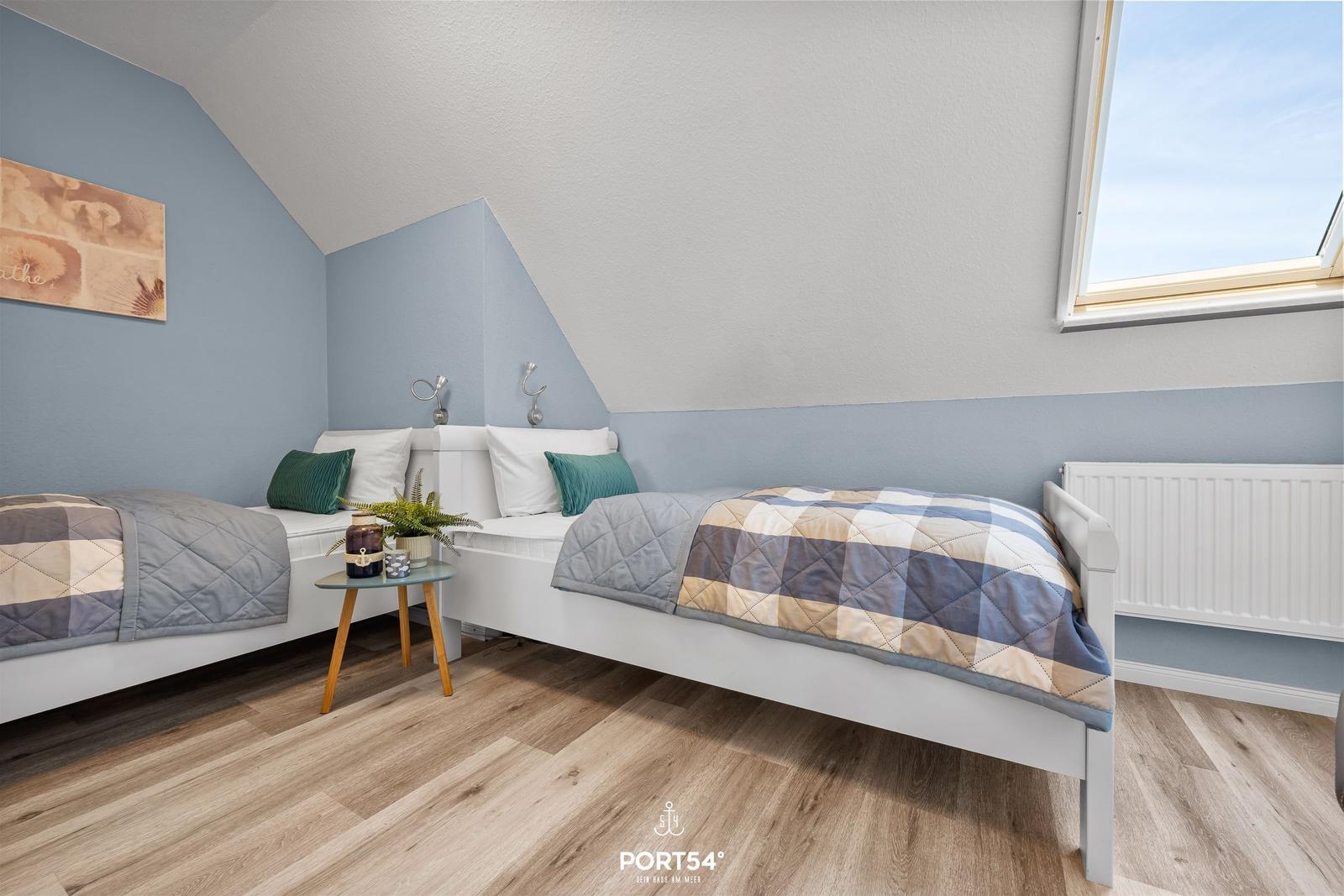 Zimmer mit zwei Betten, Holzboden und Dachfenster. Wandfarbe blau-weiß.