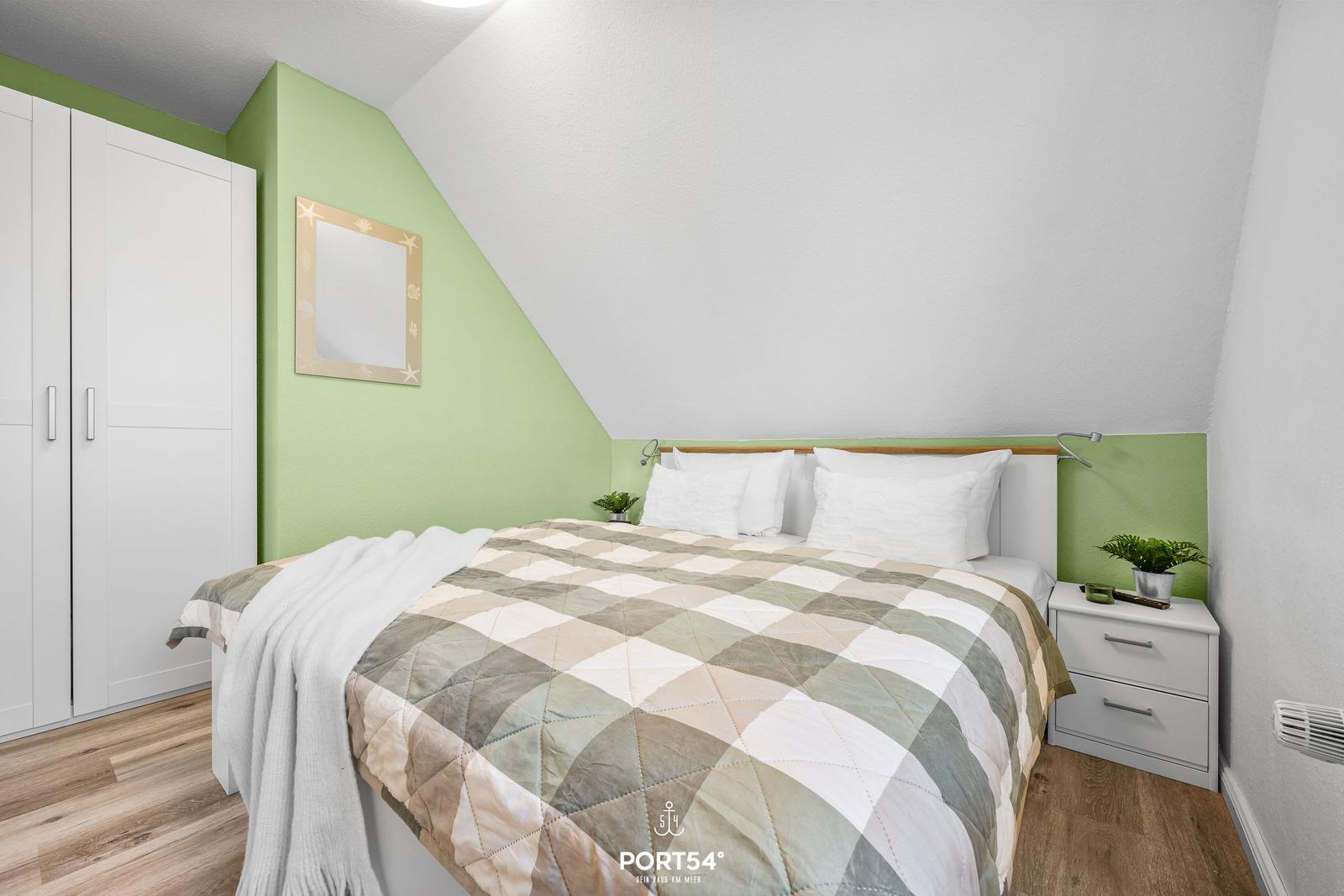 Schlafzimmer mit Bett, Kleiderschrank und Nachttisch. Wandfarbe grün, Holzboden.