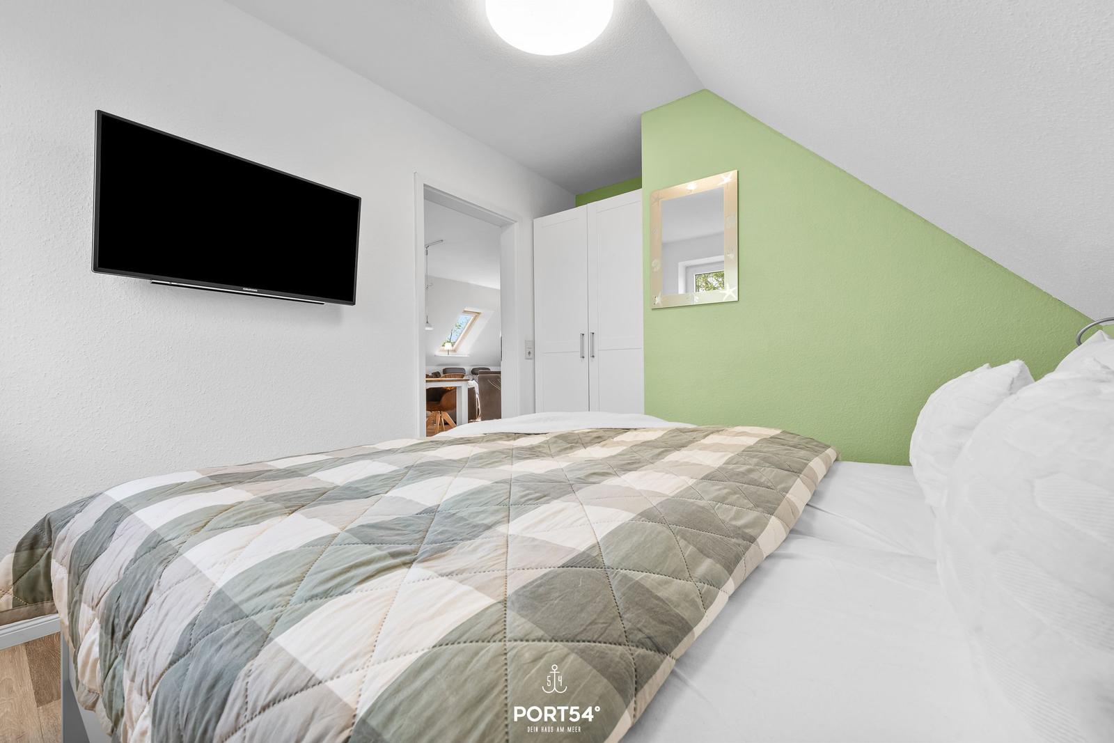 Schlafzimmer mit Bett, Fernseher und grünem Wandabschnitt