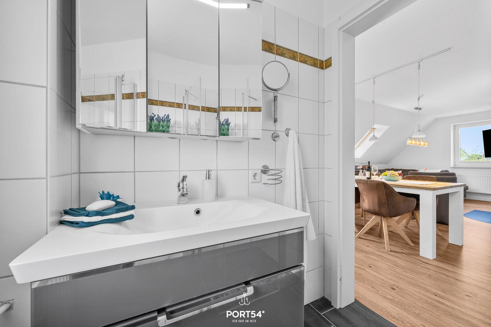 Badezimmer mit Waschbecken, Spiegelschrank und Blick in Essbereich.
