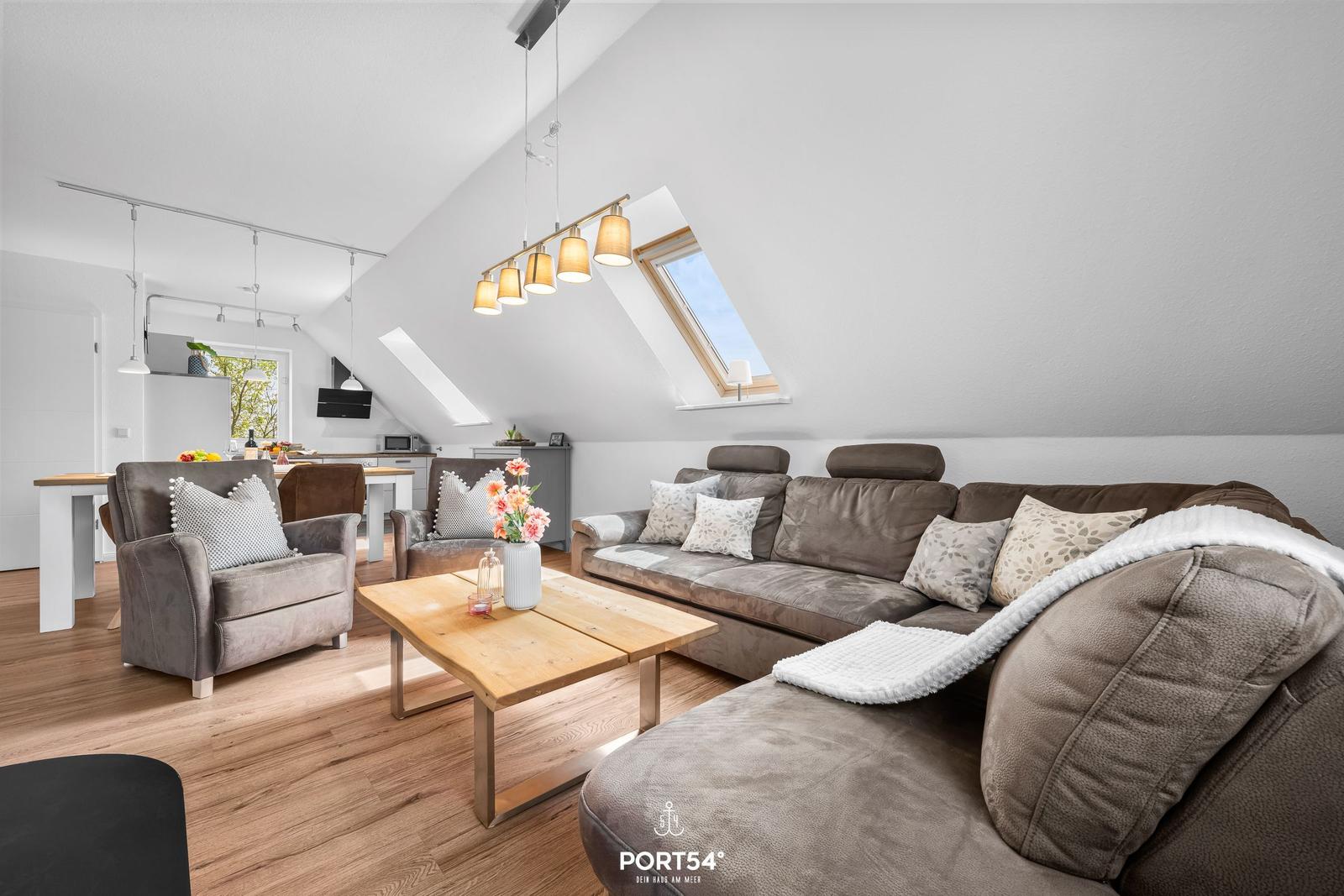 Wohnbereich mit Sofa, Sessel und Holztisch unter Dachschrägen mit Dachfenstern.
