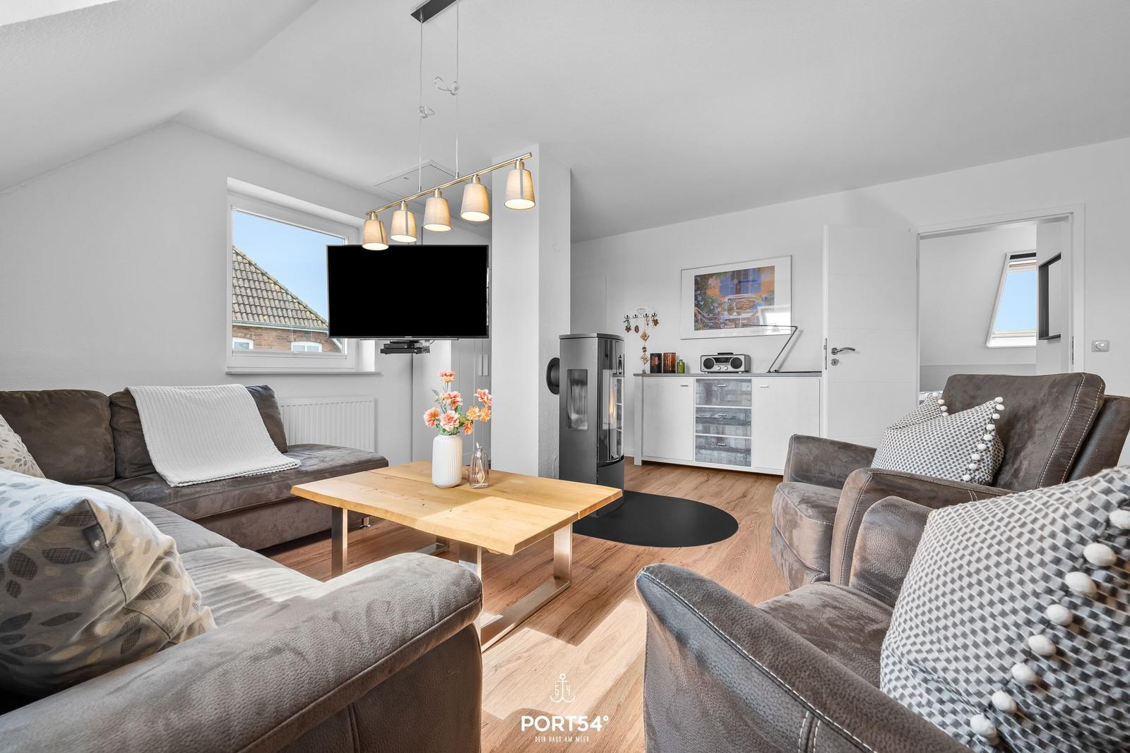 Wohnzimmer mit Sofa, Sessel, Holztisch und Fernseher an der Wand.