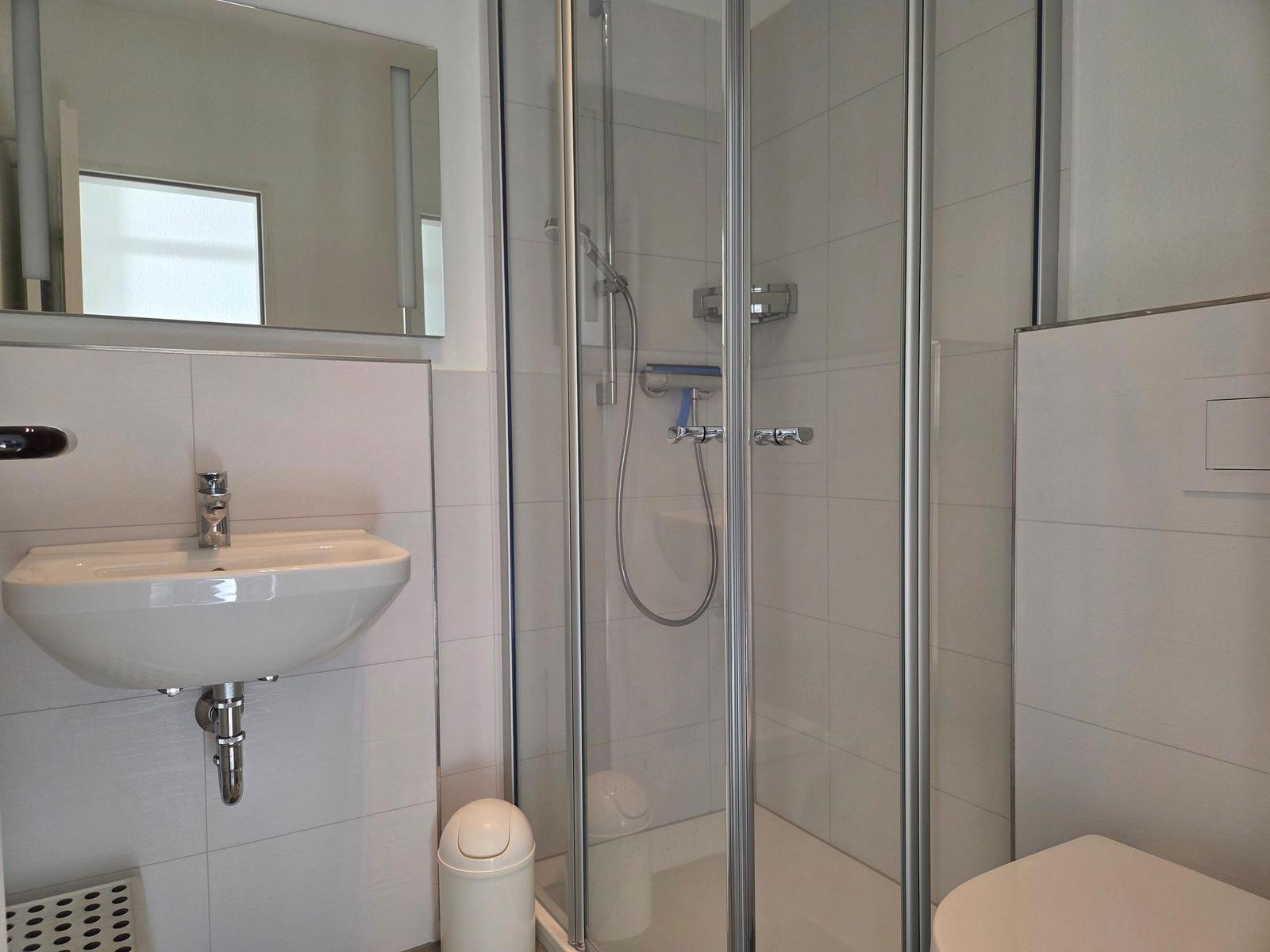 Badezimmer mit Dusche, Waschbecken und Spiegel