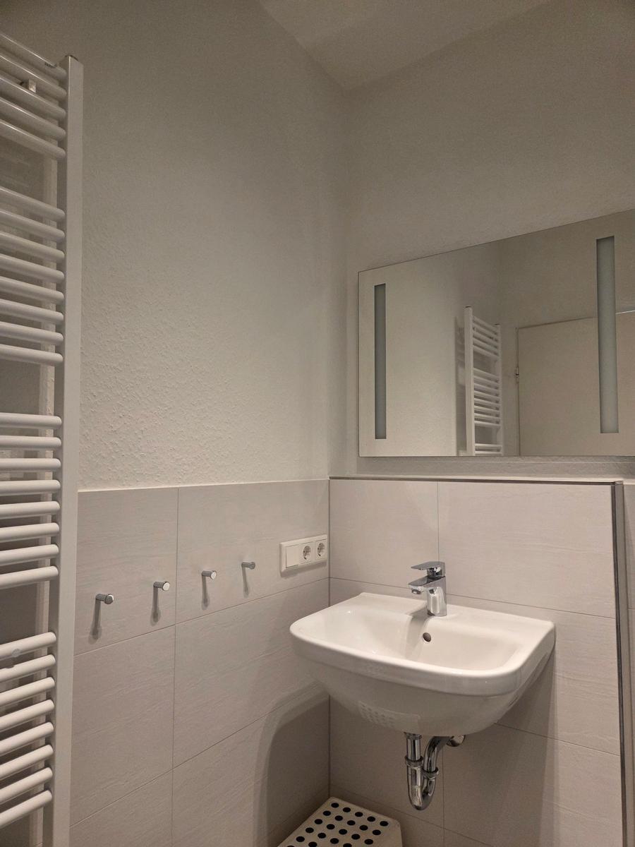 Badezimmer mit Waschbecken, Spiegel und Heizkörper an der Wand.
