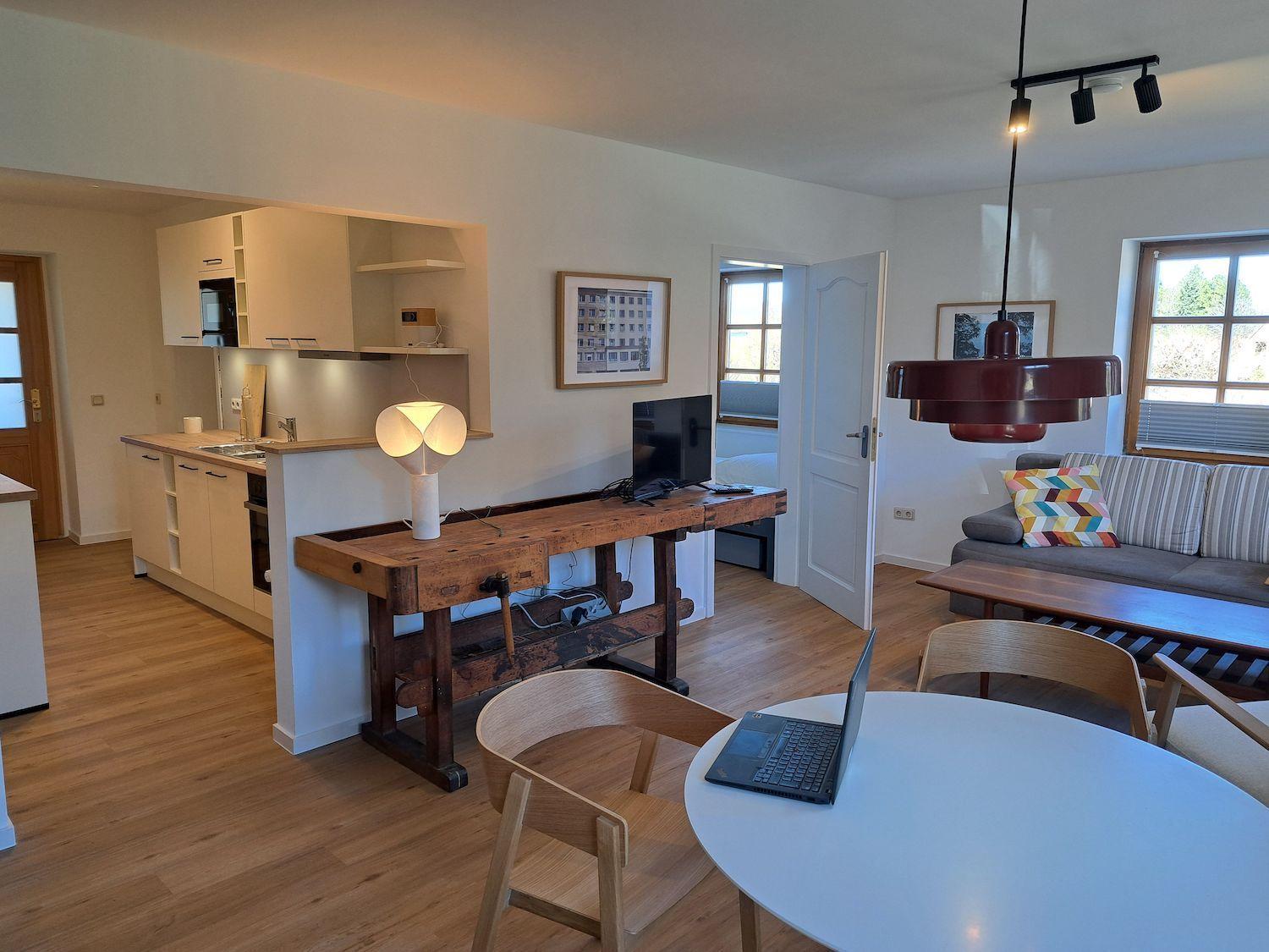 Wohnküche mit Holzboden, Sofa, Esstisch und Arbeitsplatz.