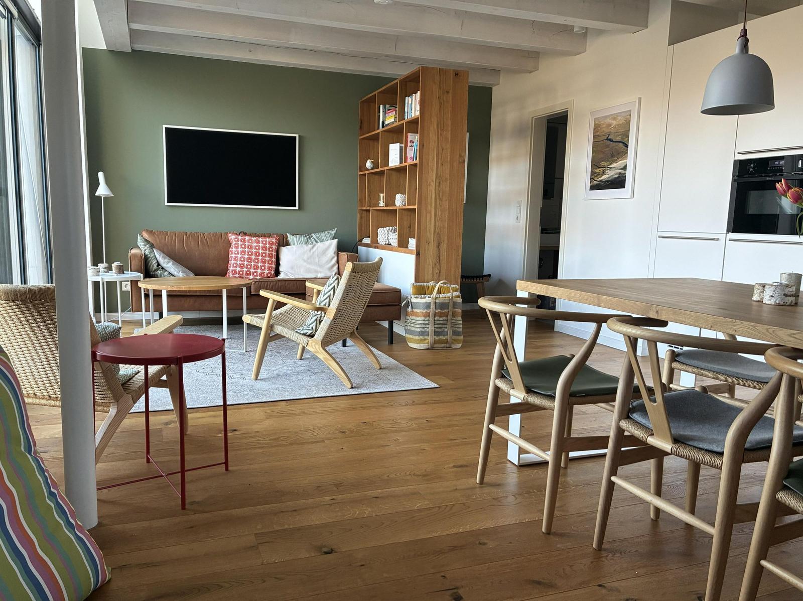Wohn- und Essbereich mit Holzboden, Sofa, Fernseher und Esstisch mit Stühlen.