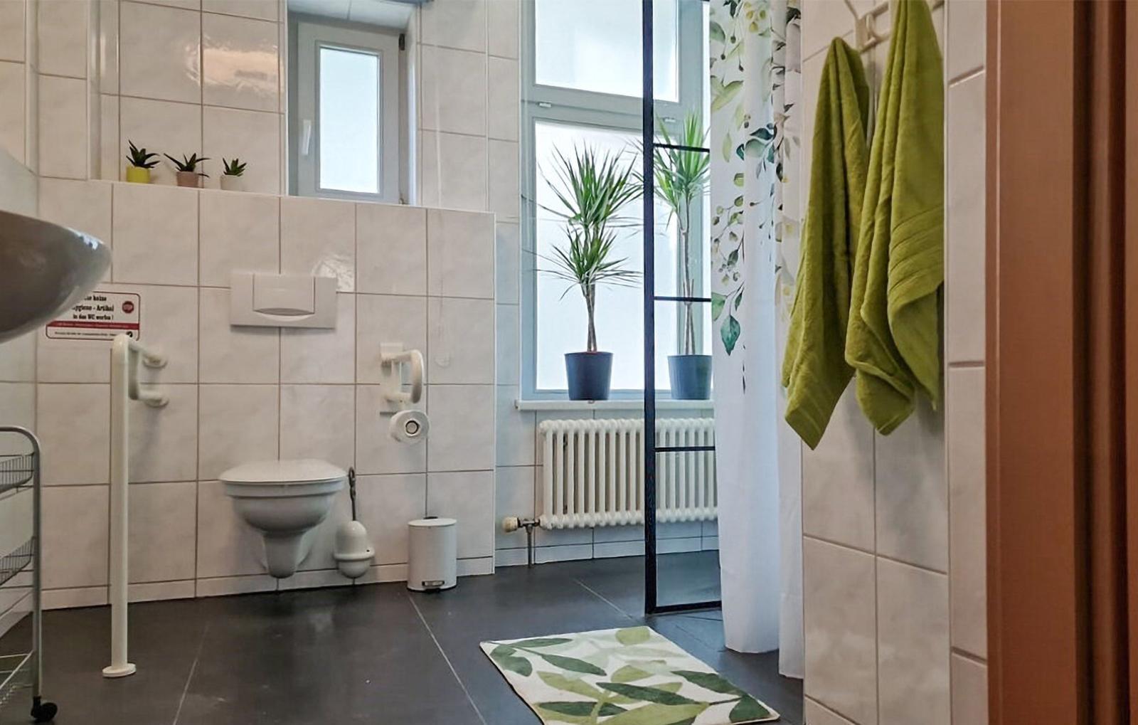 Badezimmer mit Toilette, Dusche, Fenster und grünen Handtüchern.