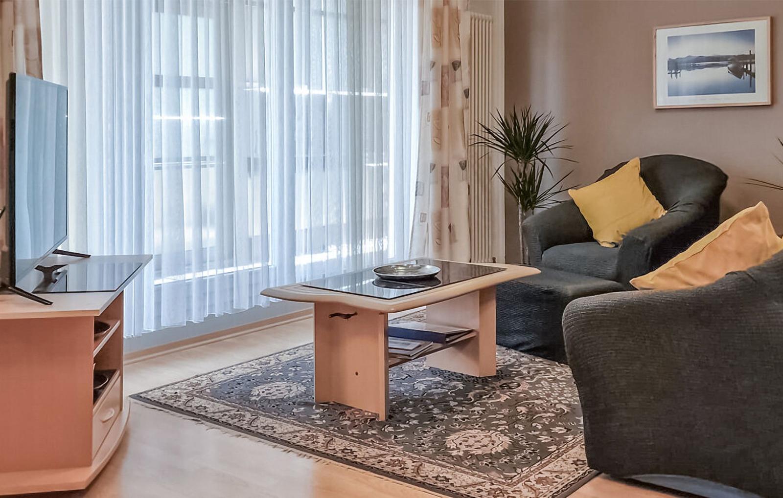 Wohnzimmer mit Sofa, Couchtisch und Fernseher. Vorhänge und Teppich sichtbar.