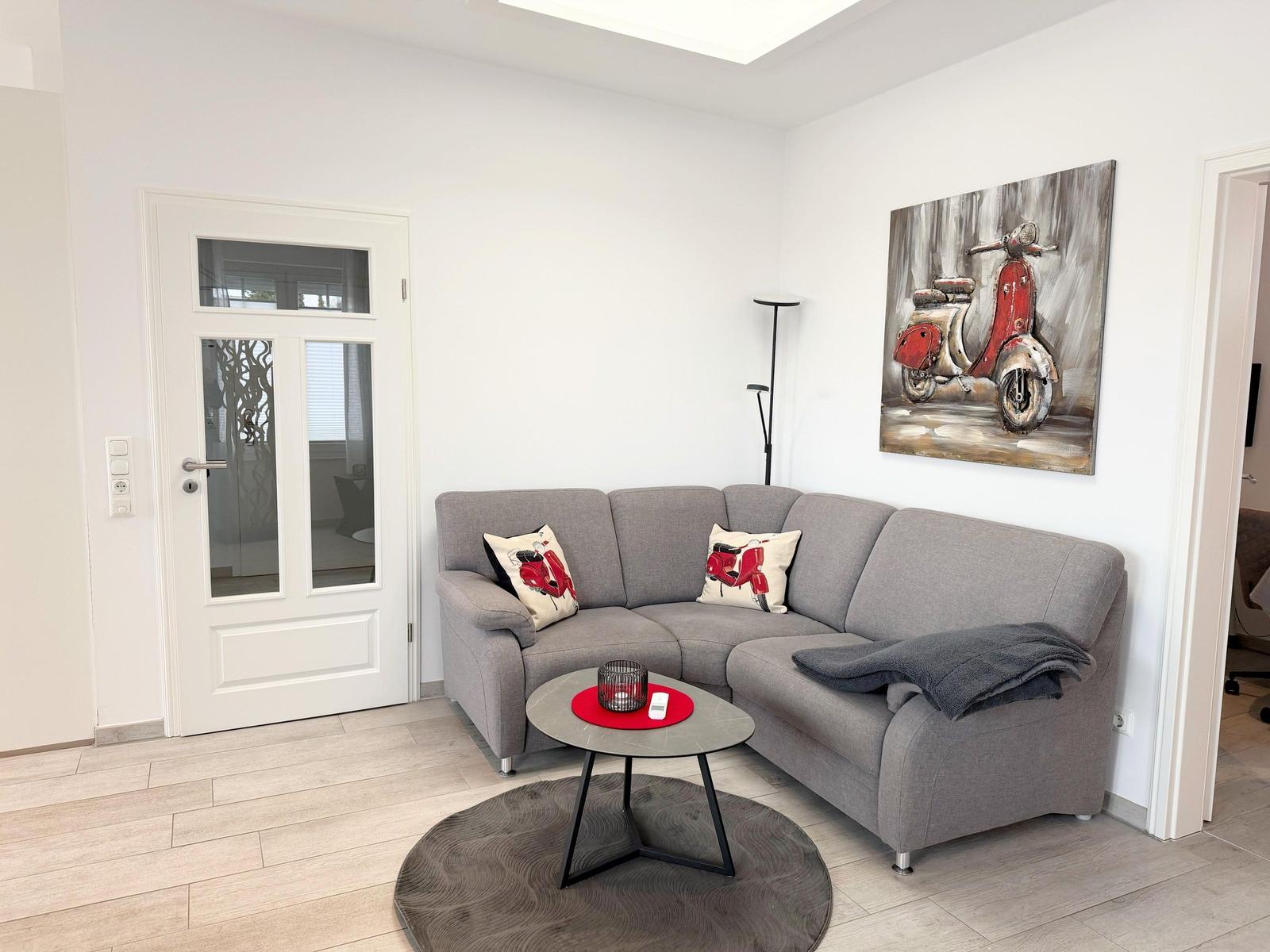 Wohnzimmer mit grauem Sofa, runden Tisch und Wandbild eines roten Motorrads.