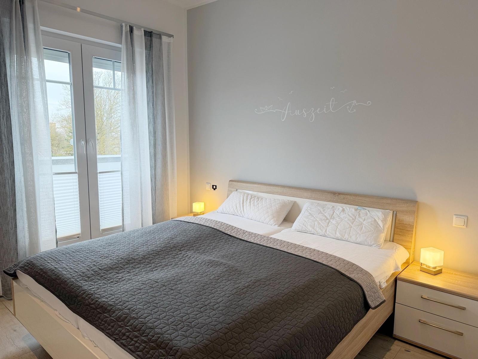 Schlafzimmer mit Doppelbett, Nachttischen und Fenster zur Terrasse.