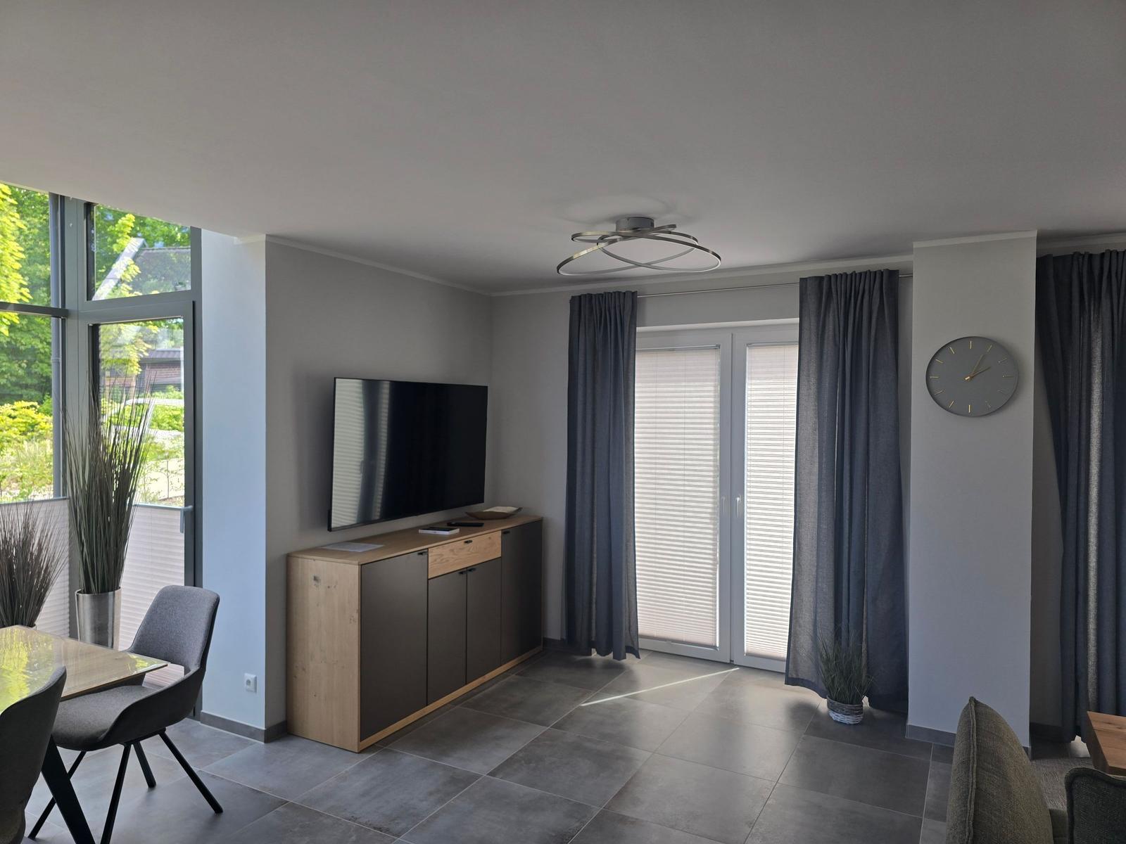 Wohnzimmer mit TV, Schrank, Fenstern und Vorhängen.