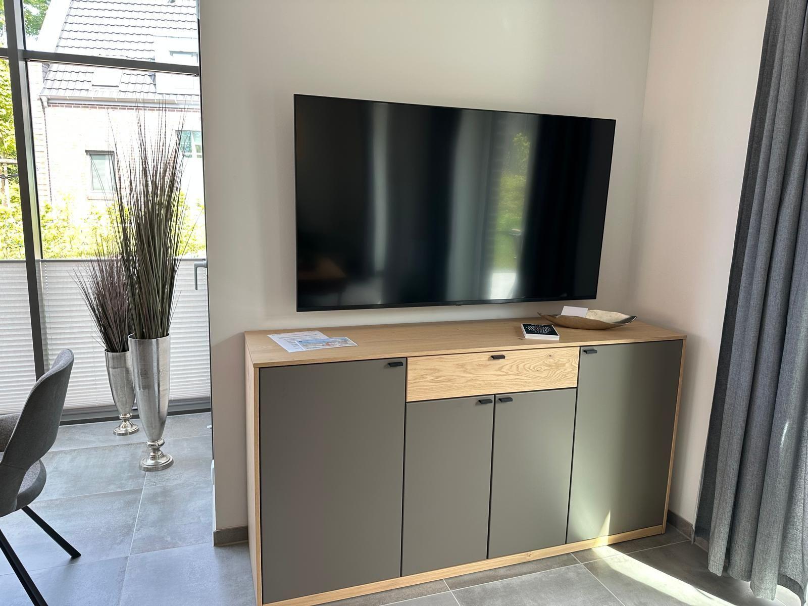 Flachbildfernseher über einem Schrank mit Holzoberfläche und grauen Türen.