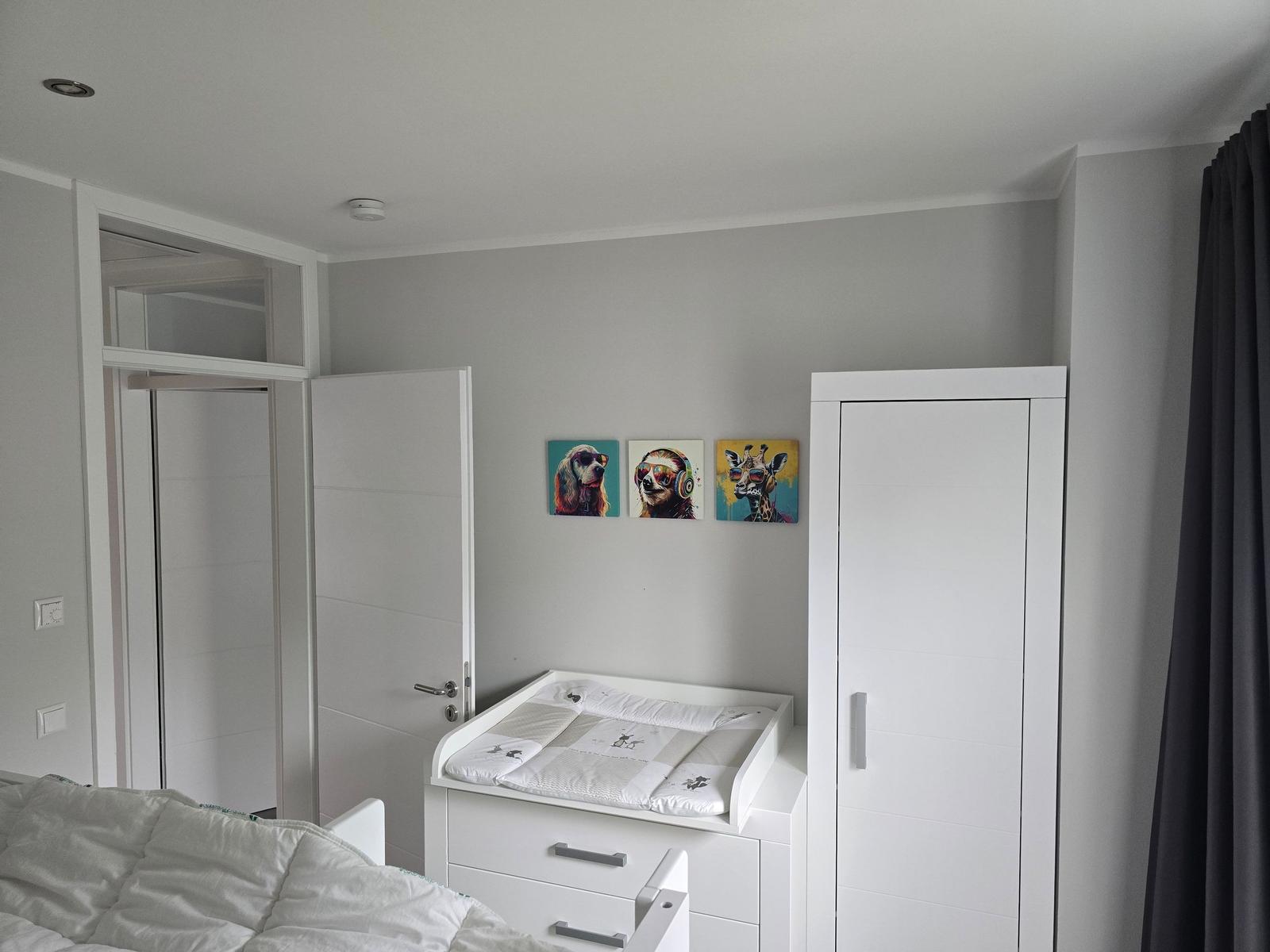 Schlafzimmer mit Wickelkommode, Kleiderschrank und Wandbildern von Tieren.
