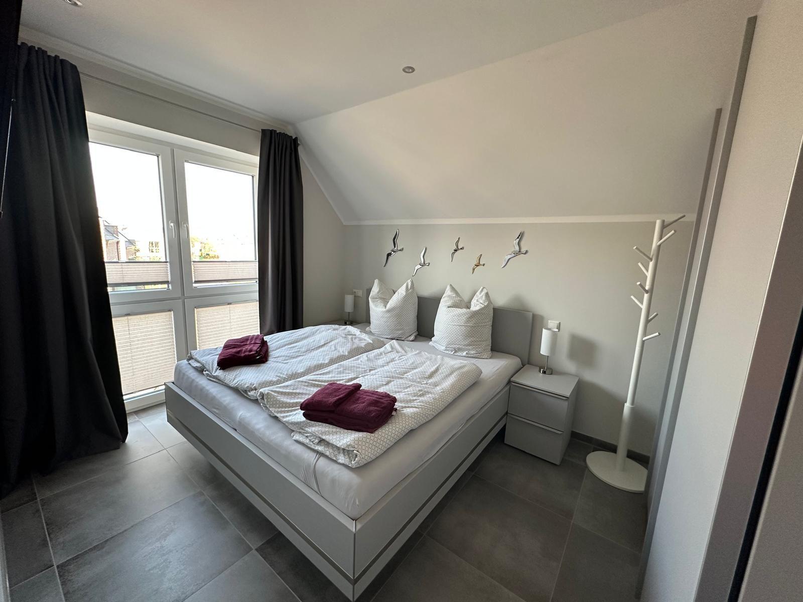 Schlafzimmer mit Doppelbett, Fenster und Kleiderständer.