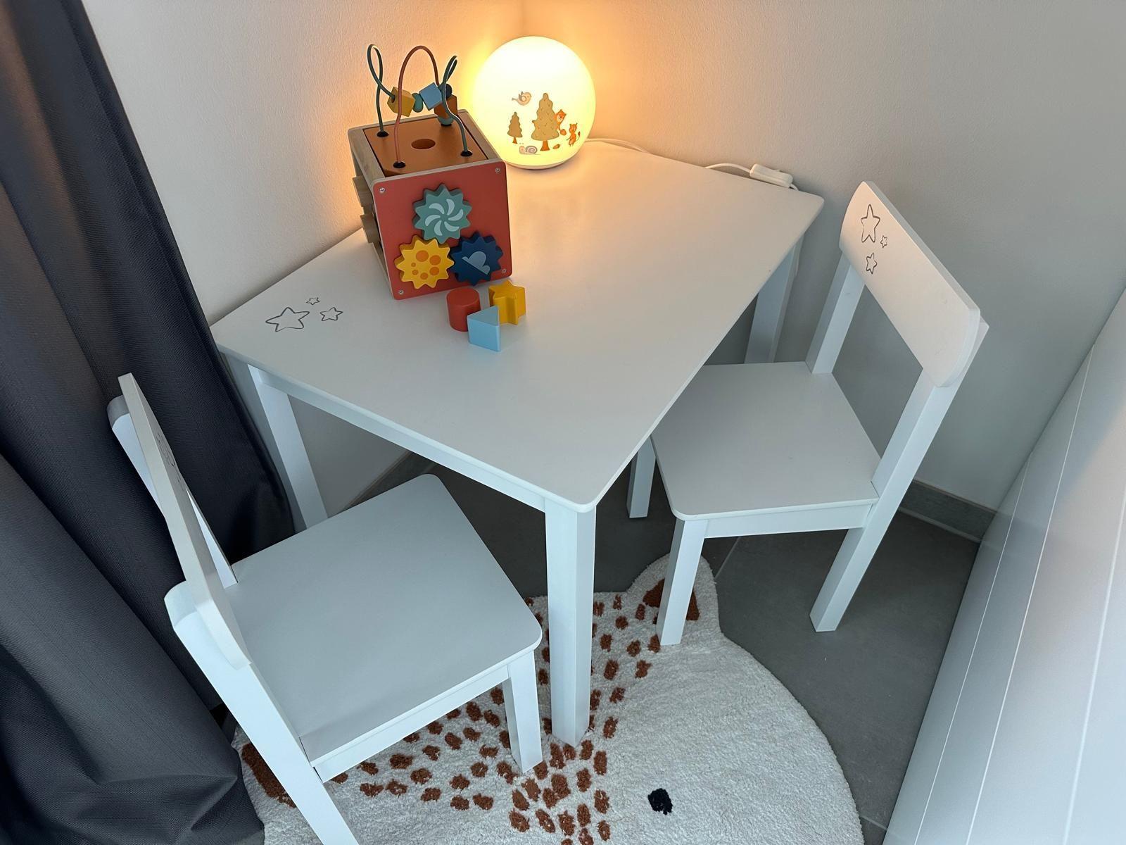 Kindertisch mit zwei Stühlen und Spielzeug auf weißem Tisch.
