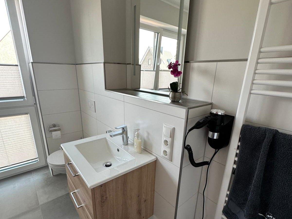 Badezimmer mit Waschbecken, Spiegel, Toilette und Heizkörper