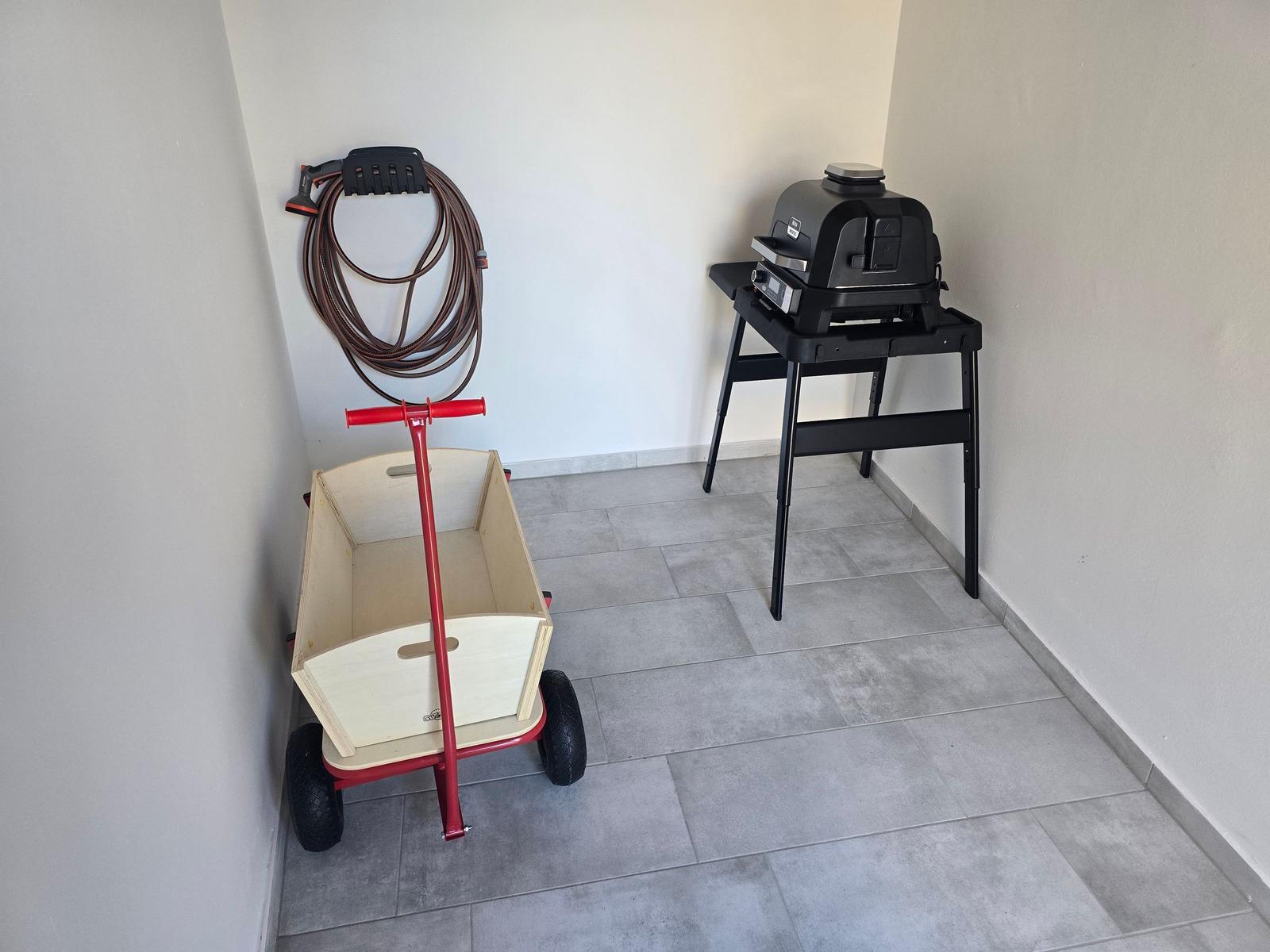 Räumlichkeiten mit Grill, Kinderwagen und Schlauch an der Wand.