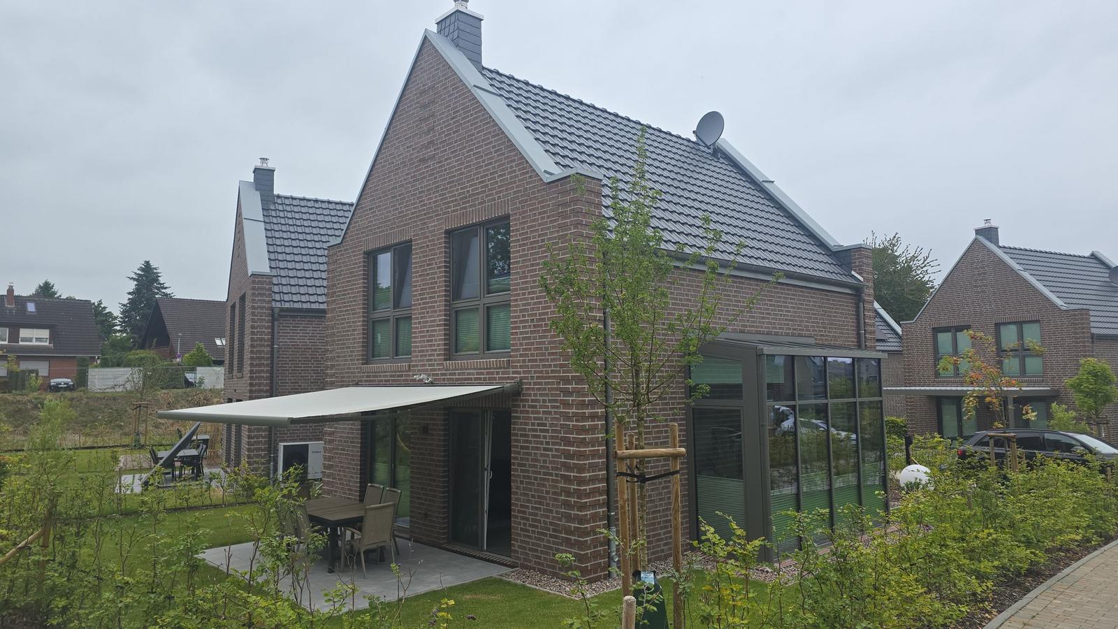 Moderne Villa mit Garten und Terrasse. Glasveranda und Holztisch sichtbar.