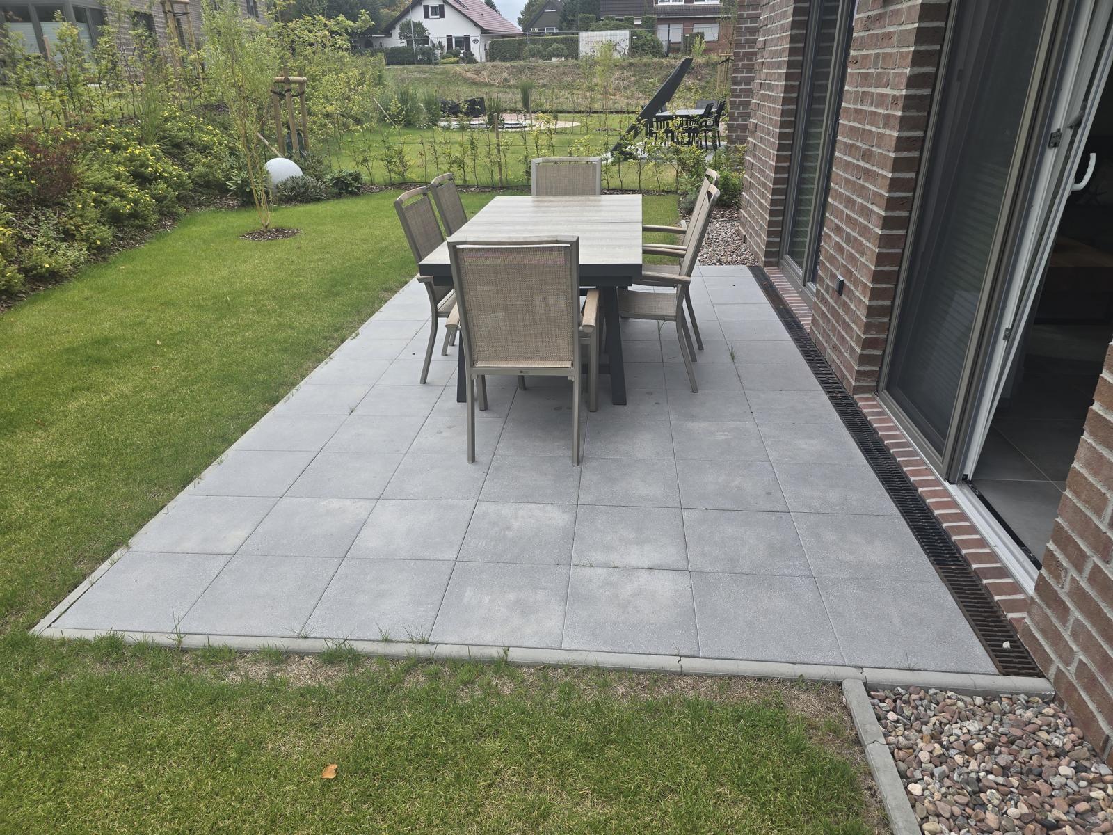 Terrasse mit Tisch und Stühlen neben Haus mit Garten.