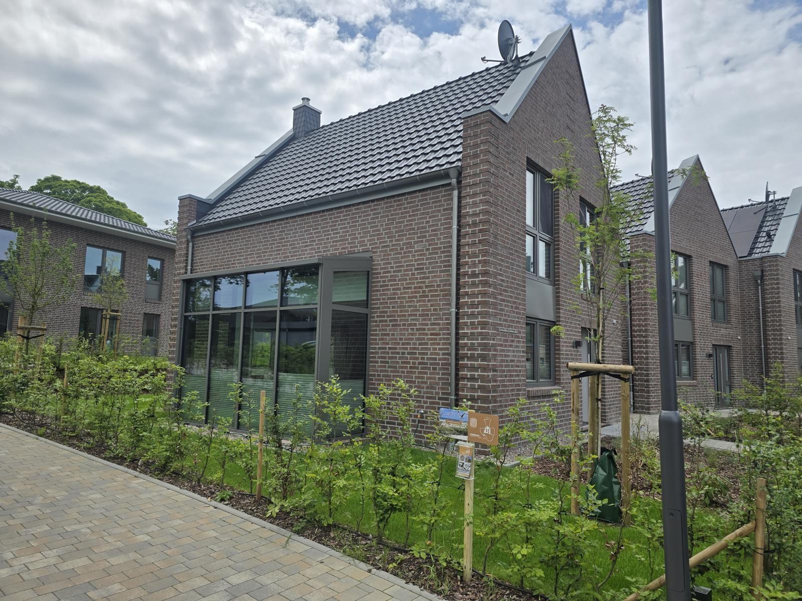 Moderne Villa mit großen Fenstern und gepflegtem Garten. Schwarzer Dachfirst und Ziegelmauer.