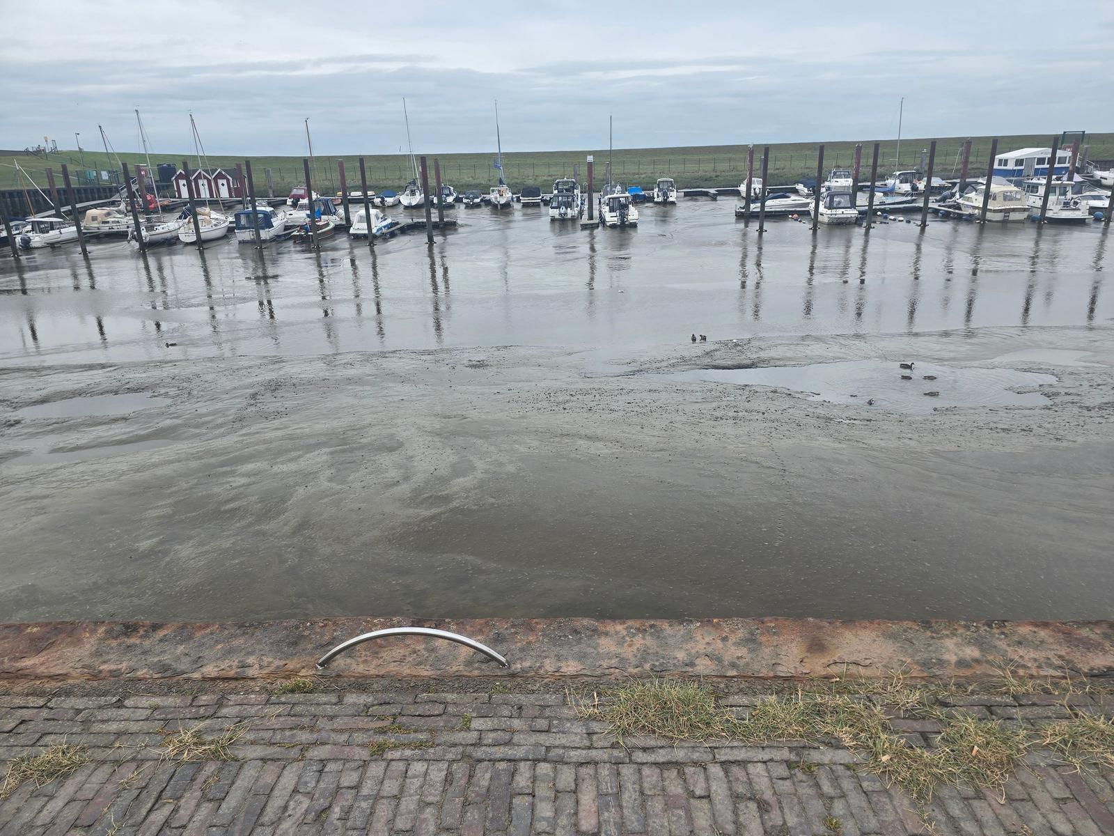 Hafen mit Booten und Watt bei Ebbe. Blick von gepflastertem Ufer.