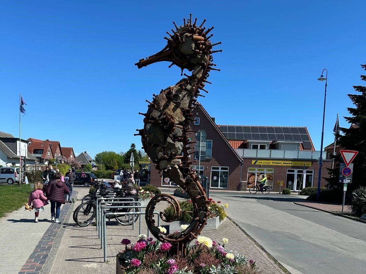 Große Metallskulptur eines Seepferdchens vor einem Markt und Fahrradstellplatz.