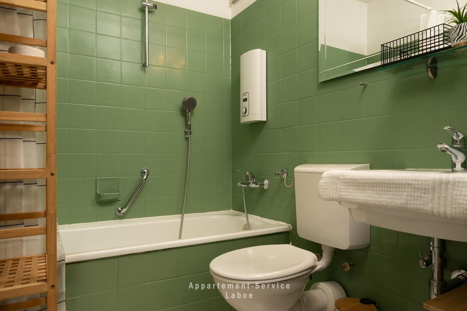 Badezimmer mit grünen Fliesen, Badewanne, Toilette und Waschbecken.