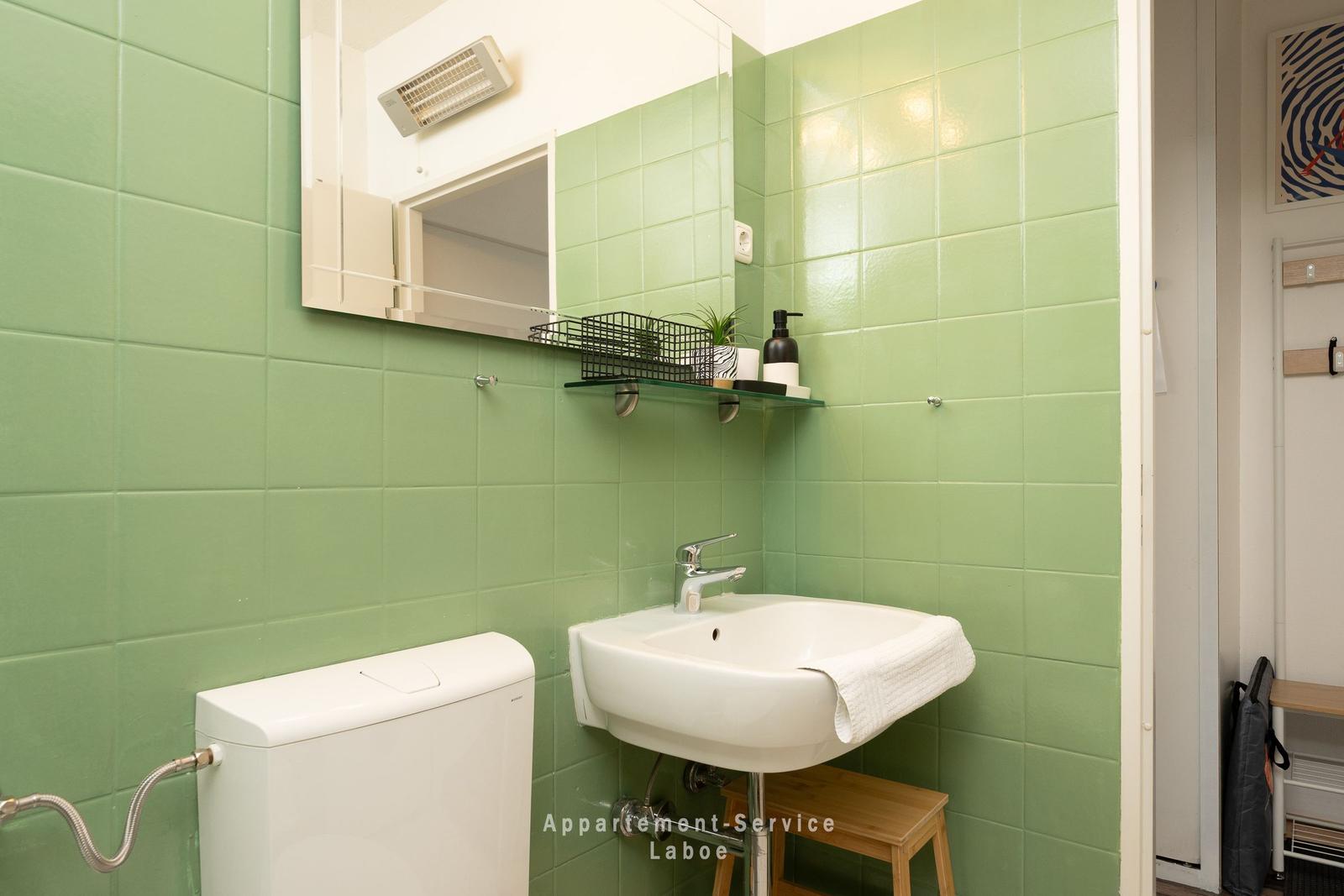Badezimmer mit grünen Fliesen, Waschbecken, Spiegel und Toilette.