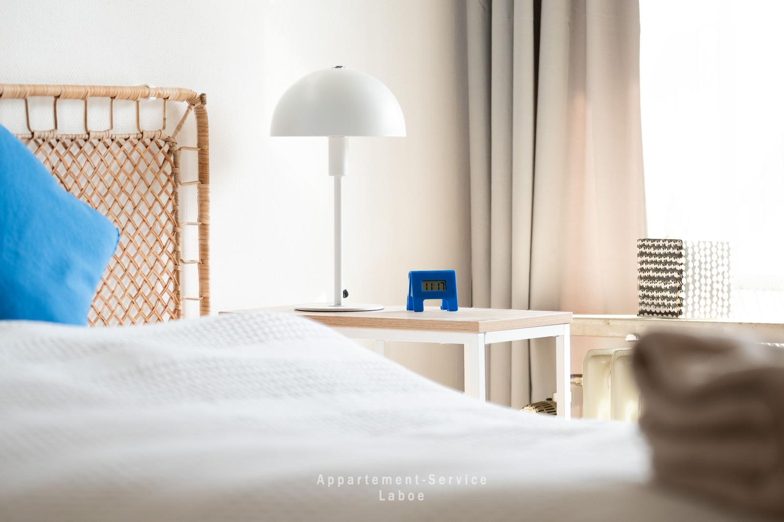 Schlafzimmer mit Bett, Nachttisch, Lampe und Wecker
