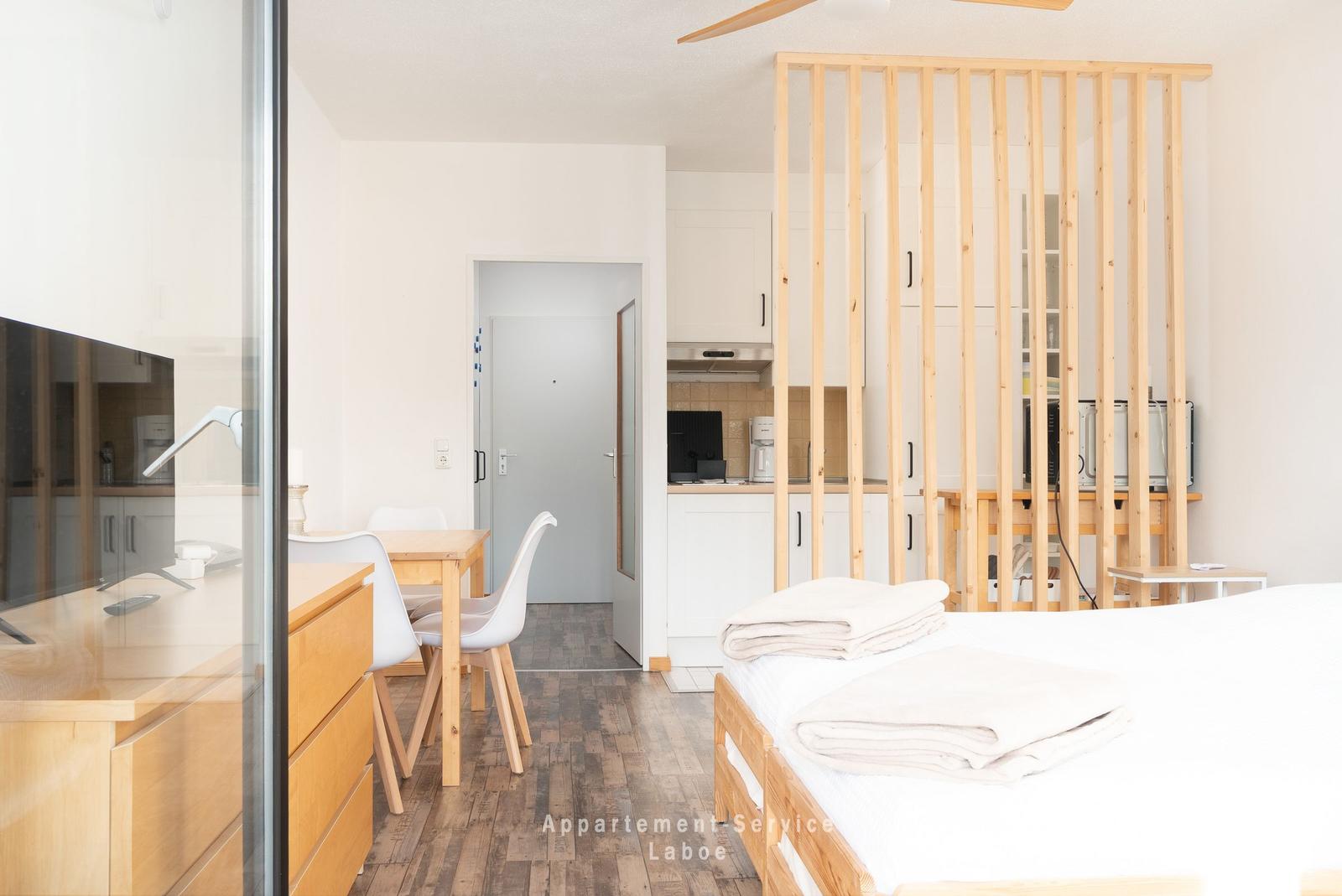 Schlafzimmer mit Bett, Holzrahmen und Blick in Küche und Essbereich.
