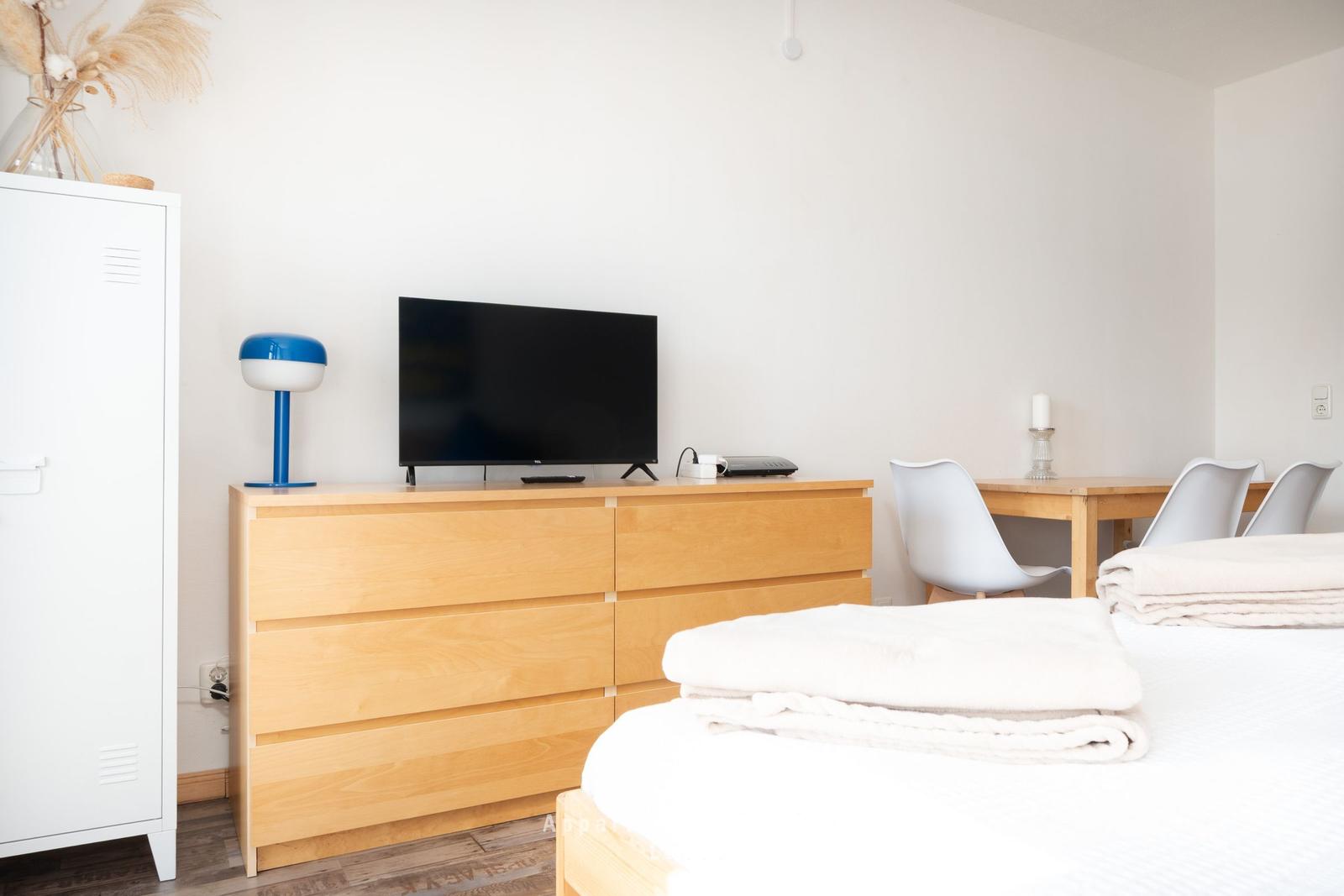 Schlafzimmer mit Bett, Schrank, TV und Esstisch mit Stühlen.