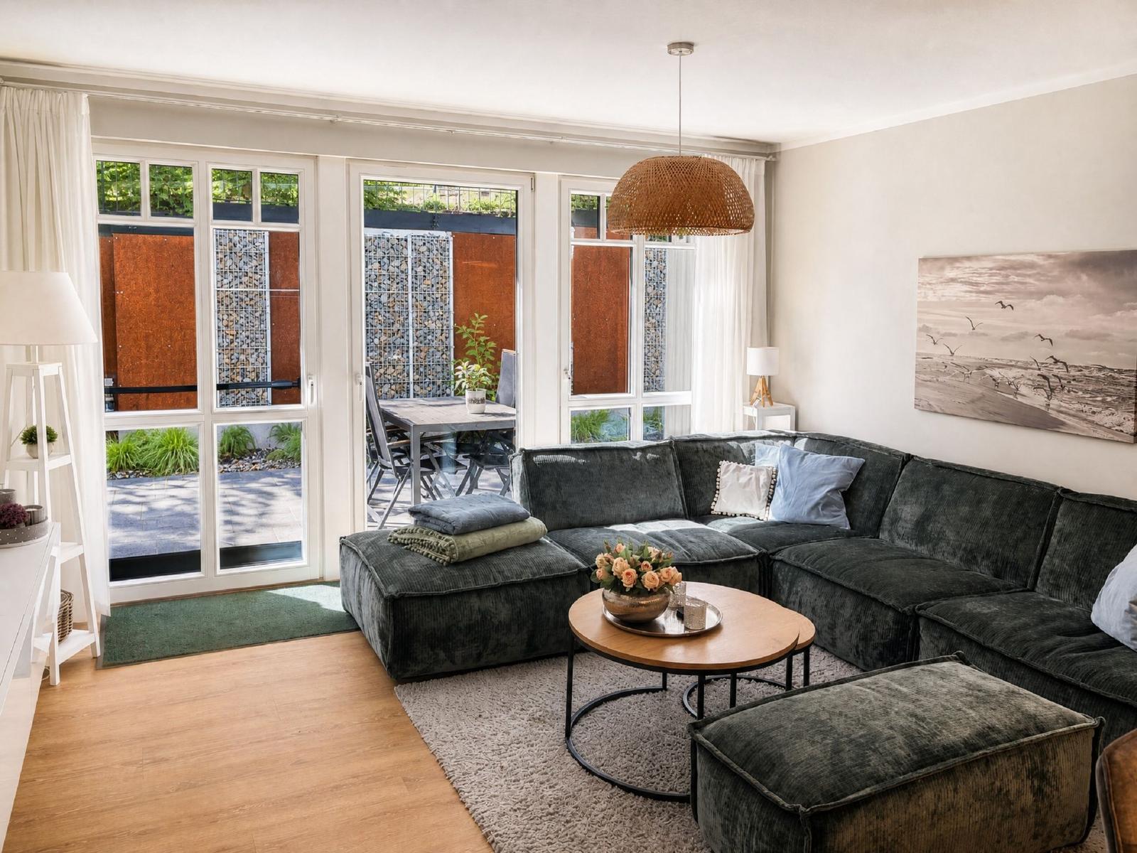 Ein Wohnzimmer mit grauem Sofa, runden Tisch und Blick auf den Außenbereich.