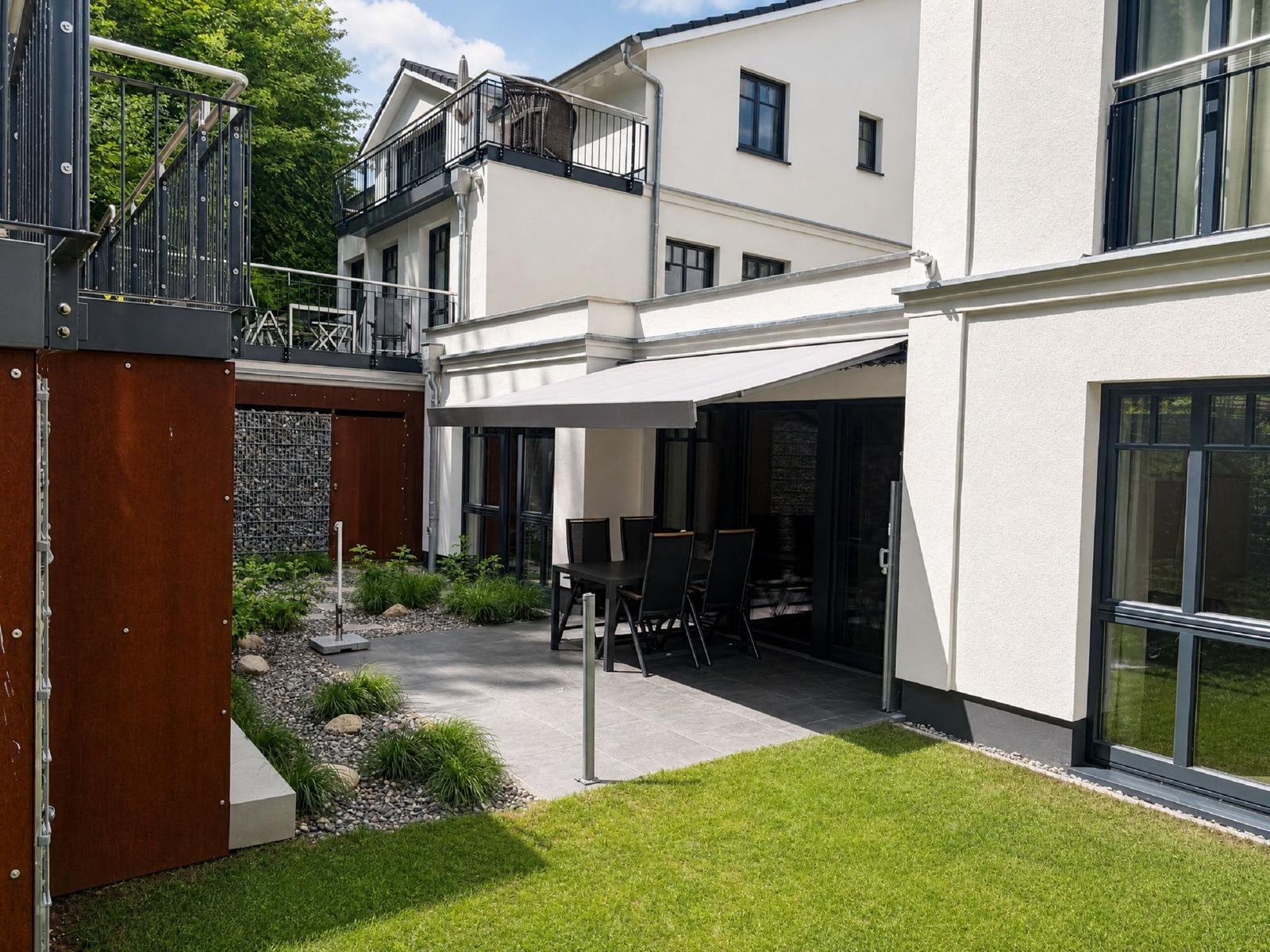 Hinterhof mit Terrasse, Sitzgelegenheit und Grünfläche. Modernes Haus mit Balkon.