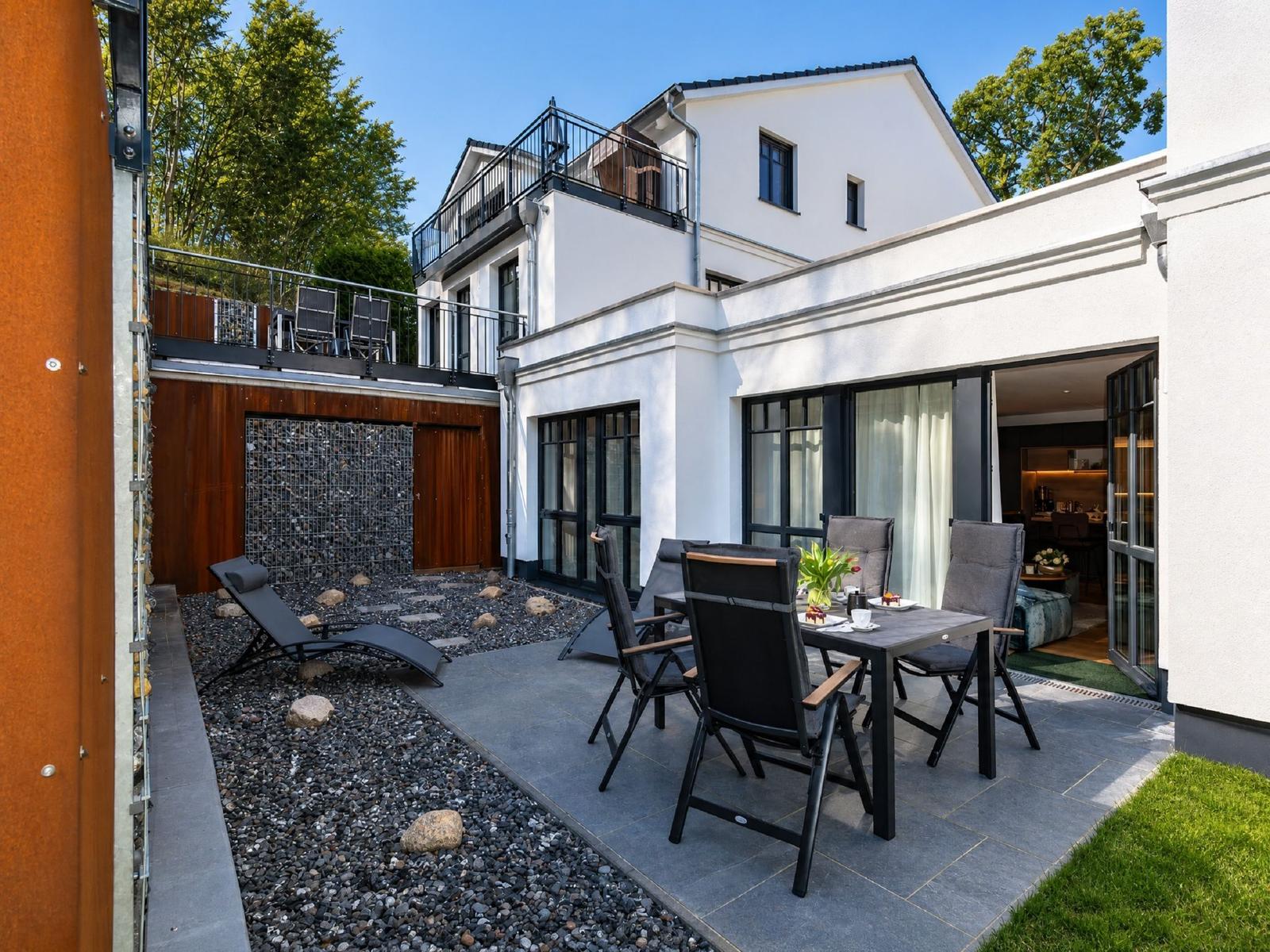 Terrasse mit Sitzgruppe, Liegestuhl und Grillbereich. Hinterhof mit Steinplatten und Grünfläche.