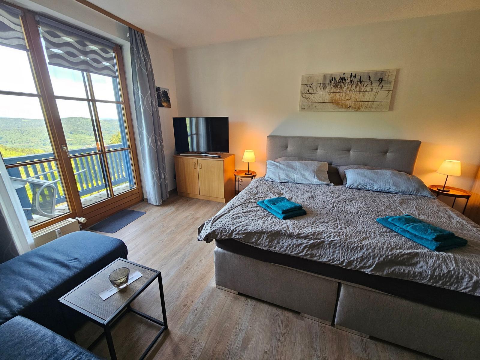 Bedroom with balcony view. Bed, TV, and nightstands.